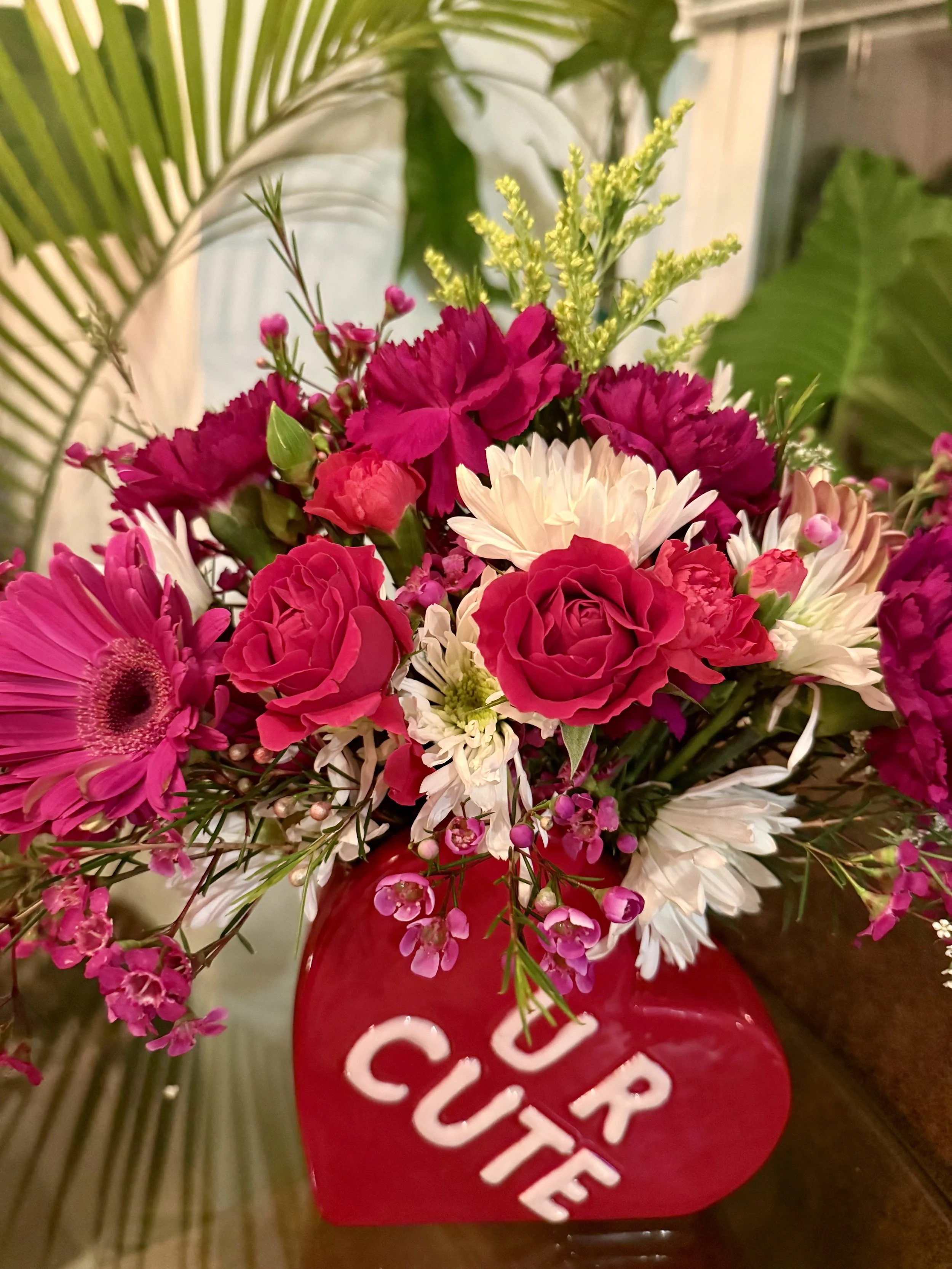A bouquet of pink, white, and red flowers in a red vase with the words "YOUR CUTE" written on it.