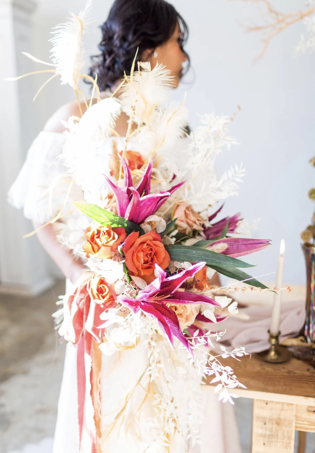 A woman holding a large bouquet of colorful flowers, including orange roses, pink lilies, white feathers, and various greenery.