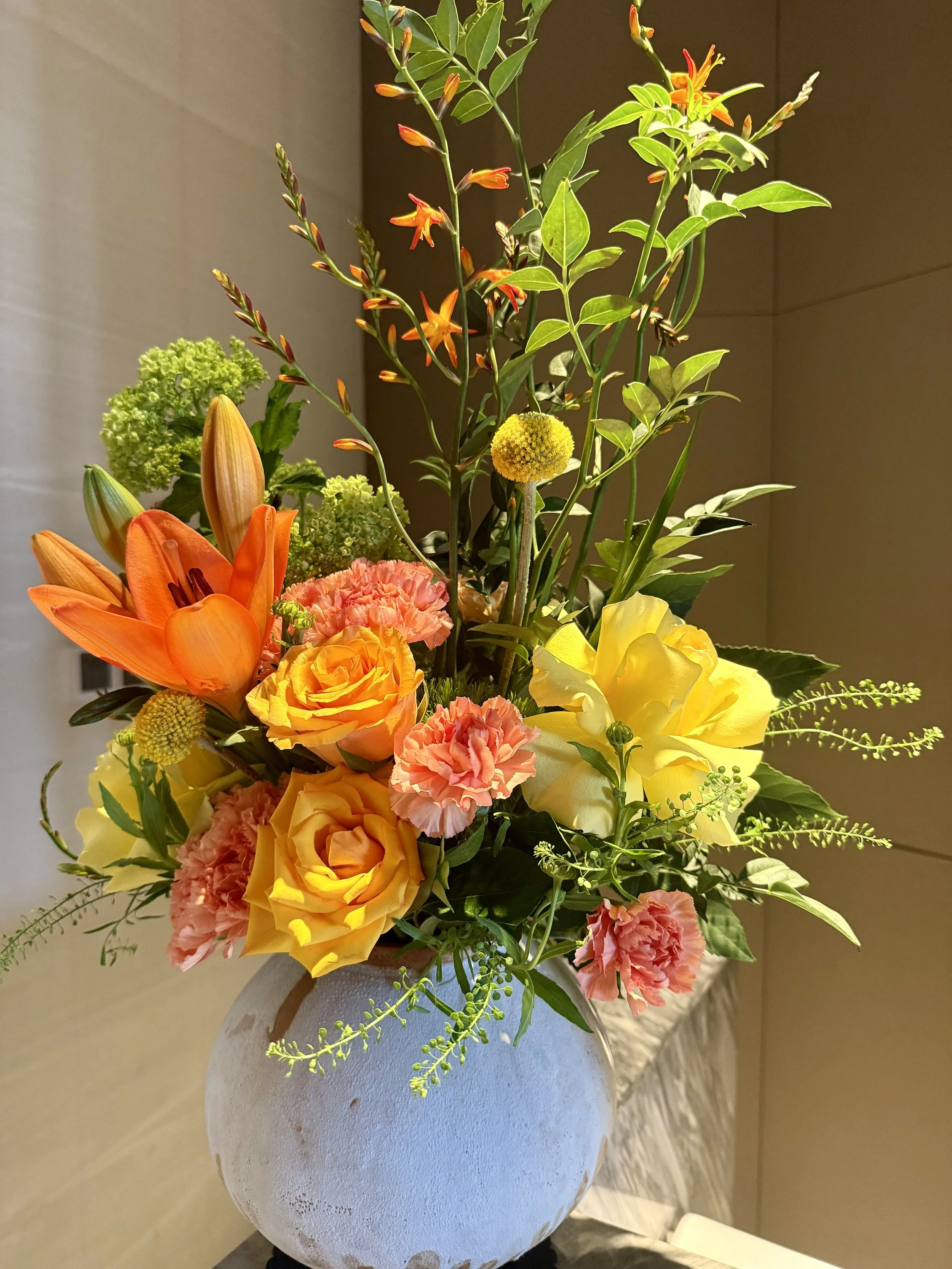 A bouquet of various colorful flowers in a white textured vase on a table.