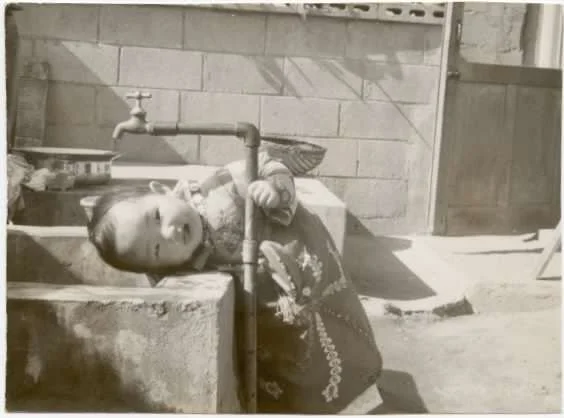 Sandy as a child, drinking from an outdoor faucet.