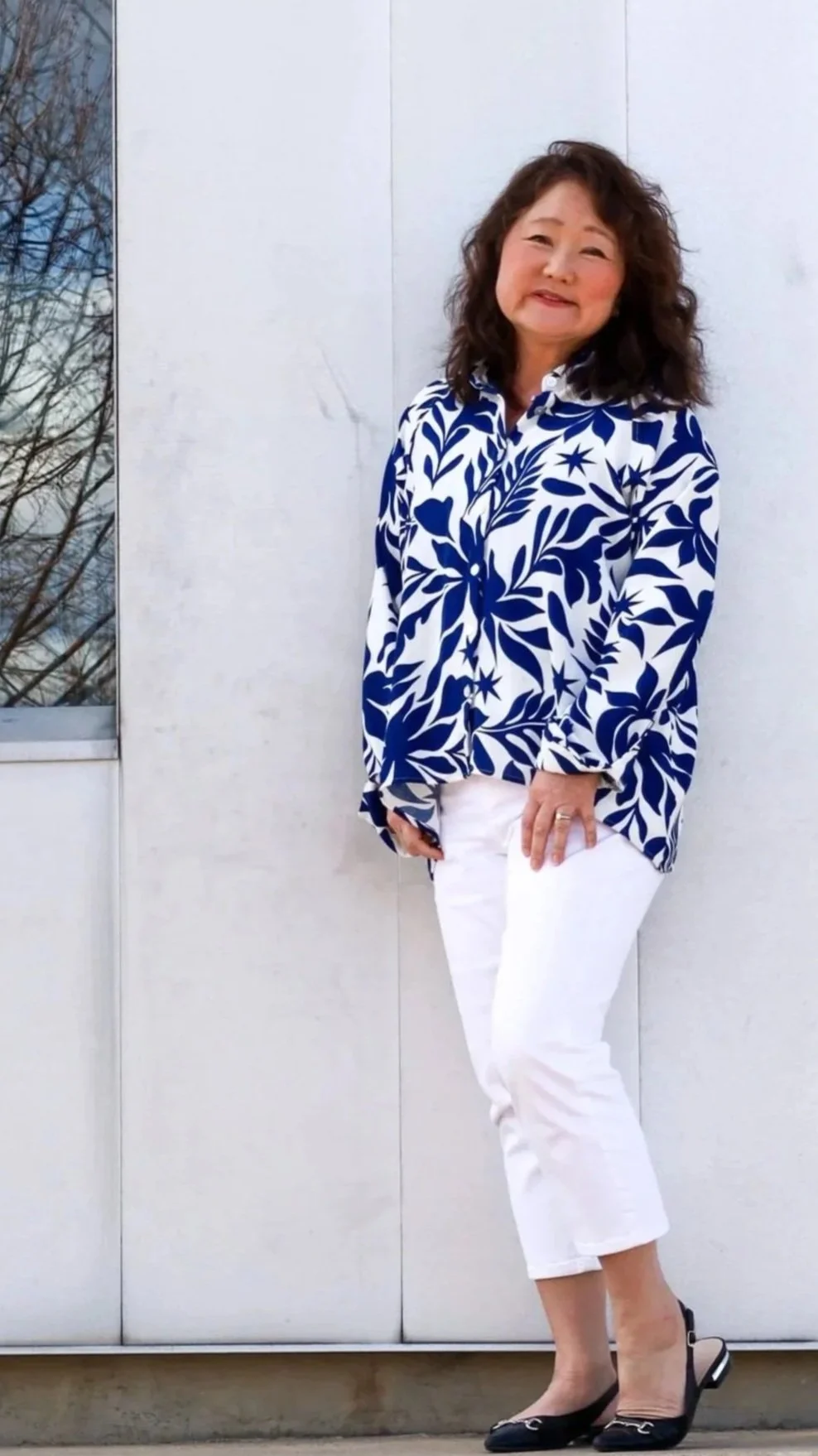 Sandy standing in a blue blouse and white pants.