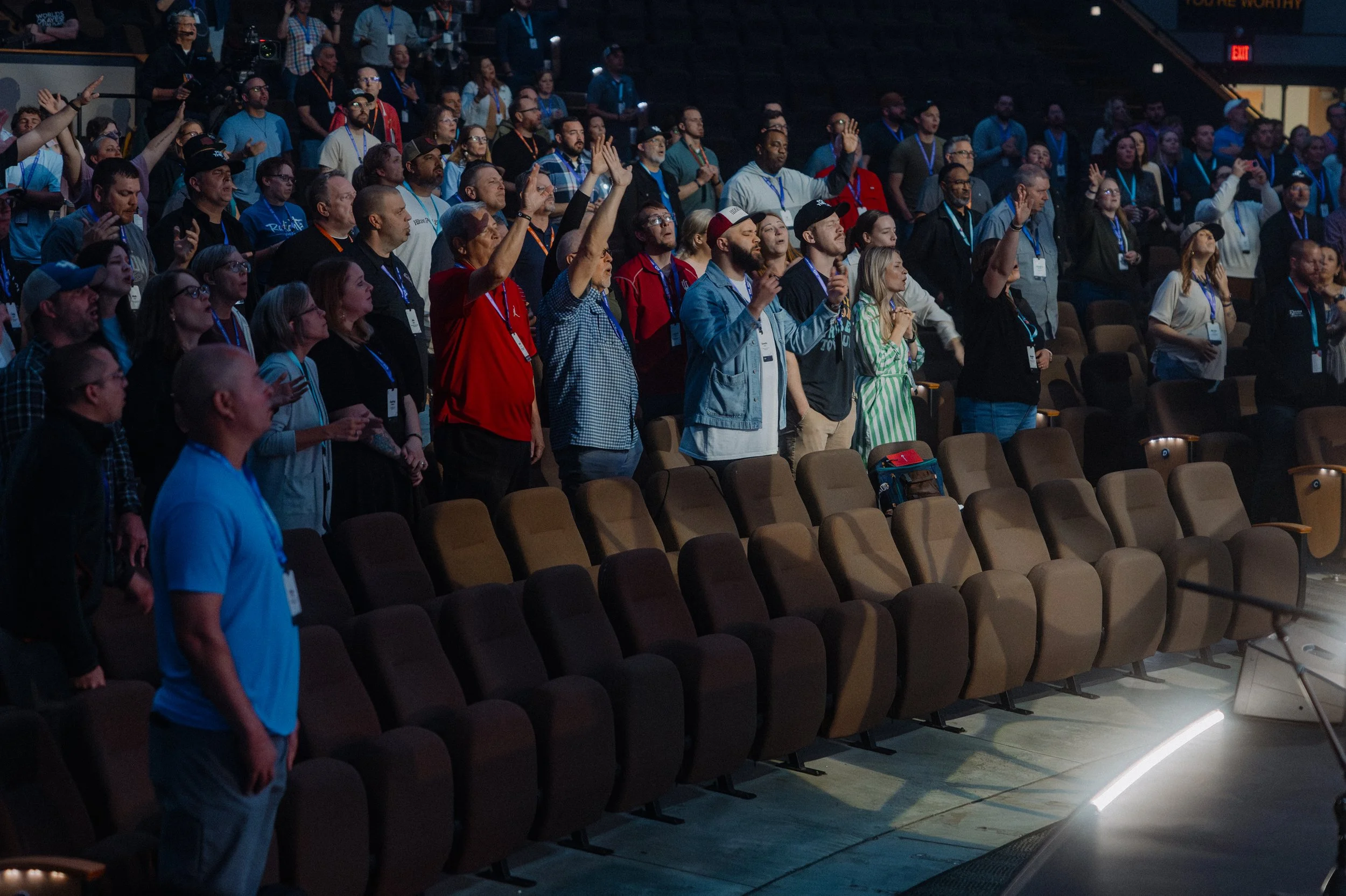 Audience members standing and raising their hands at a conference or event in a large auditorium.
