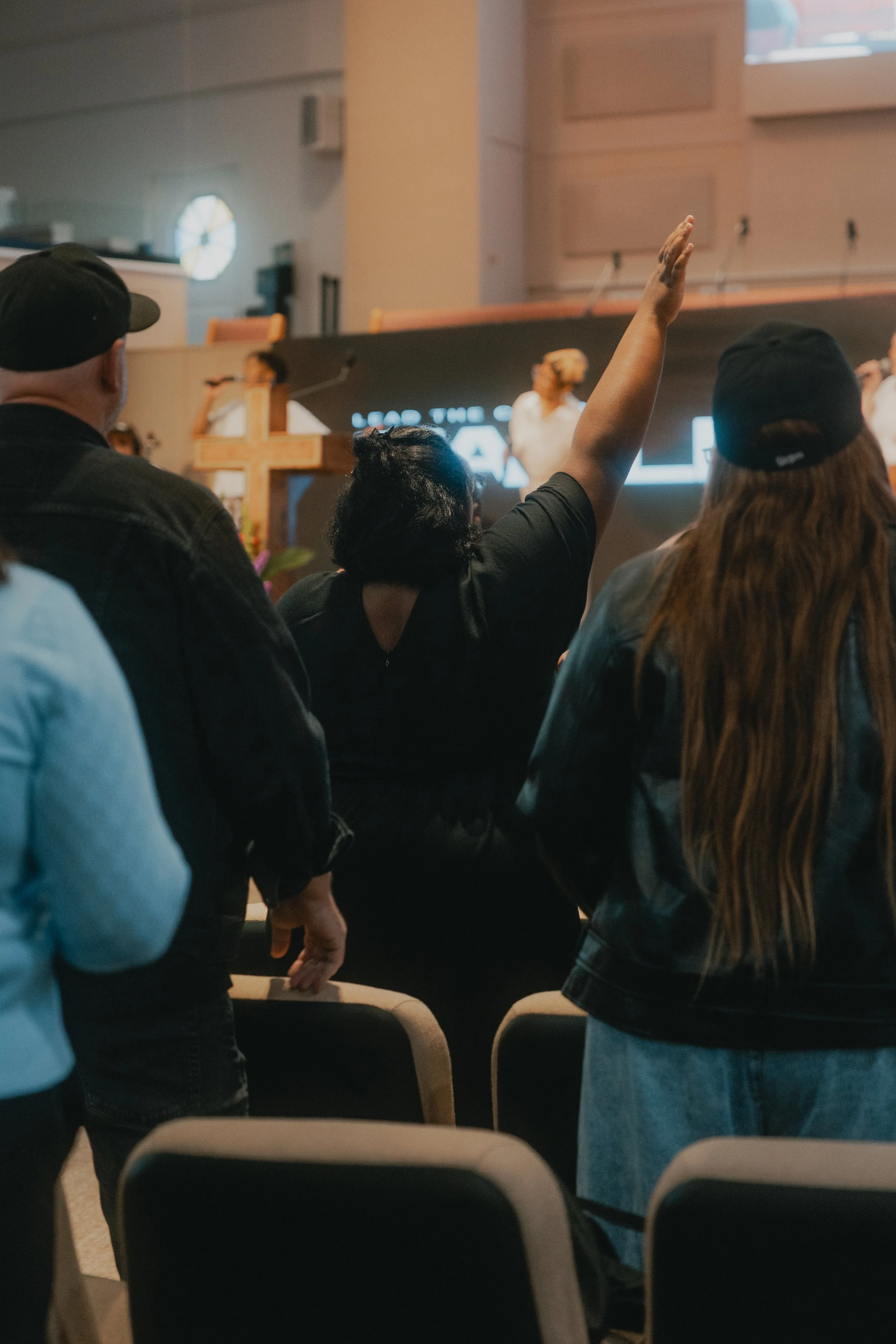 A woman raising her hand during a church service, with a cross and a digital screen visible at the front of the room.