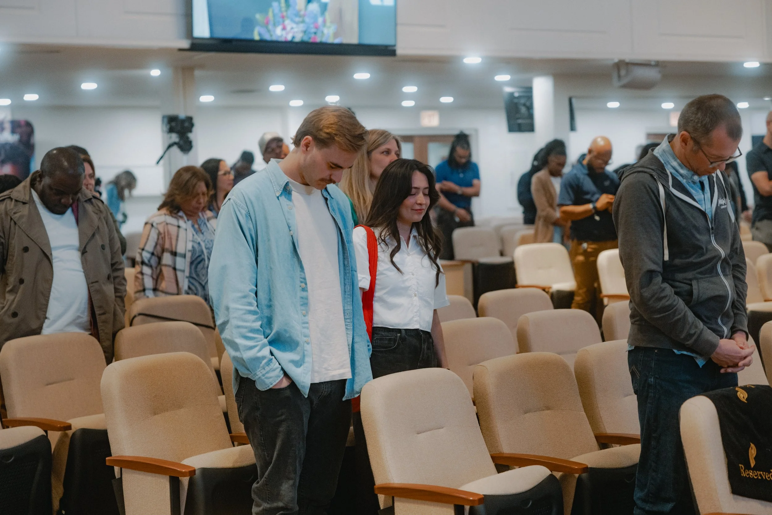 People praying inside a church, standing with heads bowed and eyes closed.