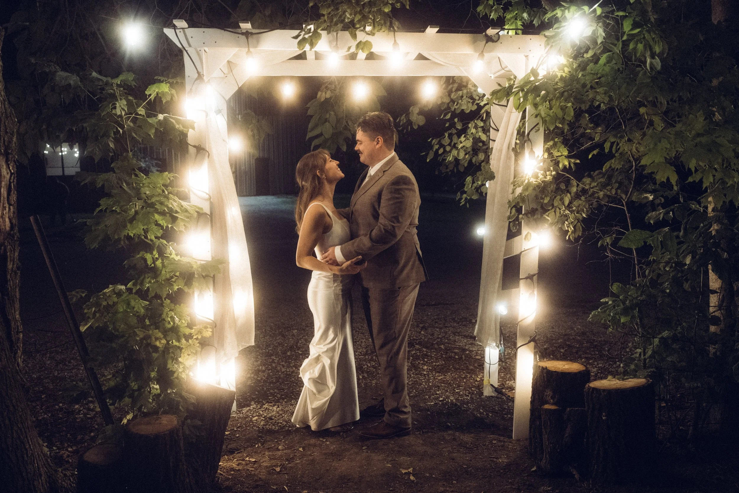 A couple dancing under a decorated archway with string lights at night.