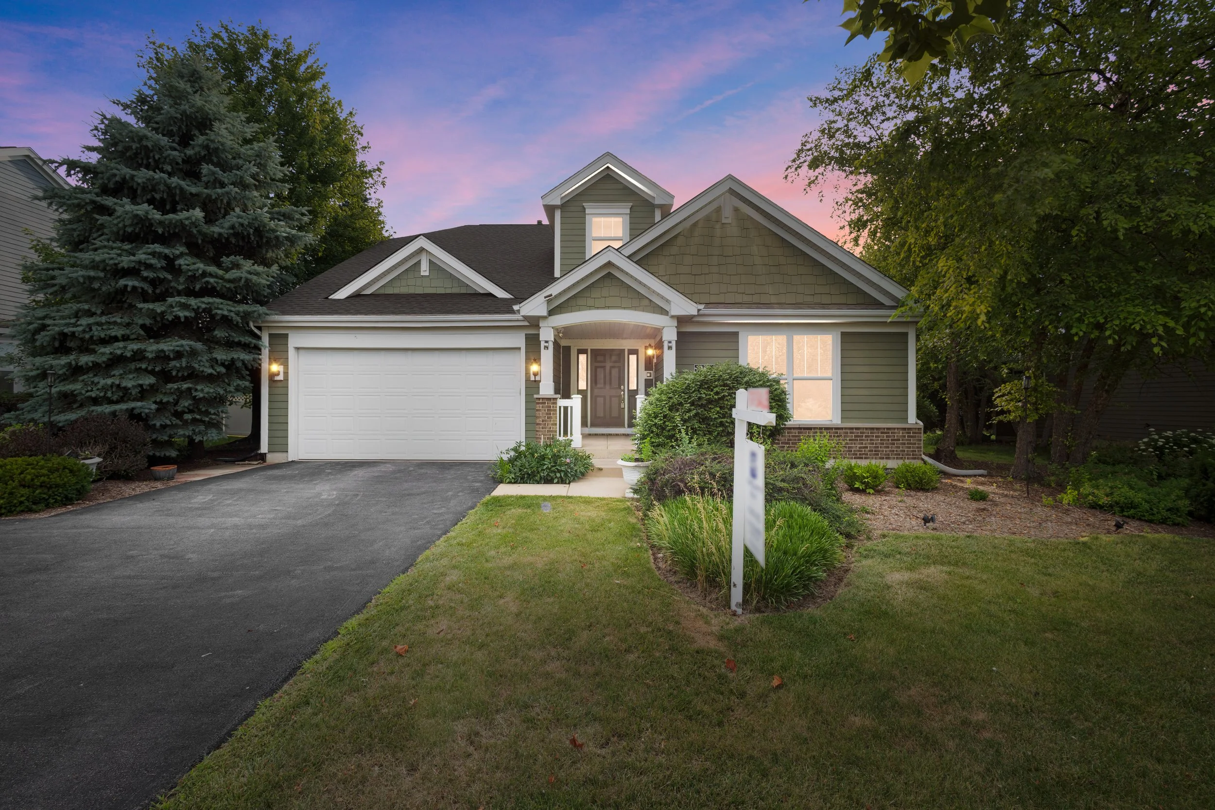 Front view of a suburban house with a dark front door, cream chimney, white garage door, and a well-maintained lawn and garden, under a sunset sky.