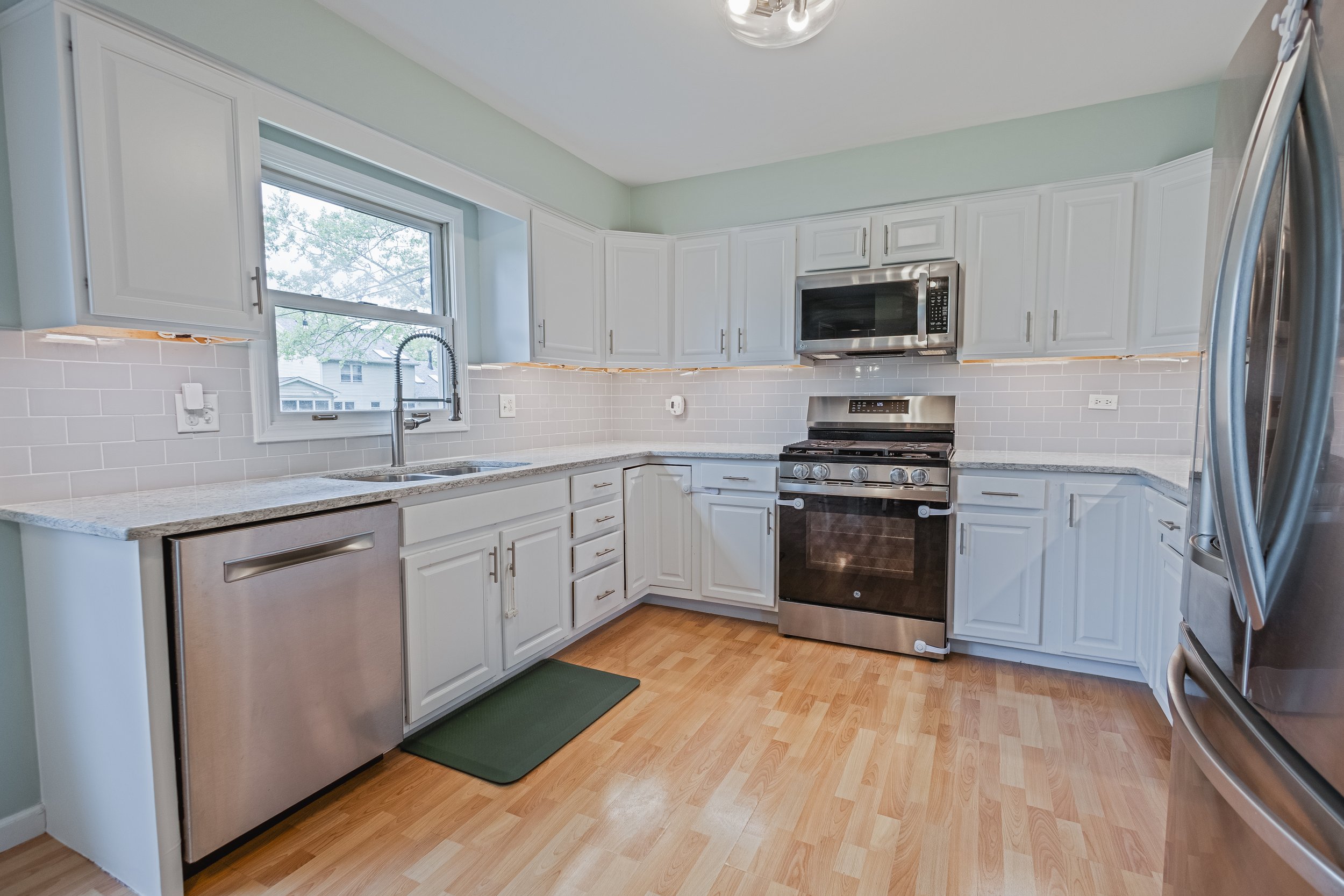Modern kitchen with white cabinets, stainless steel appliances, granite countertops, a window over the sink, and hardwood floors.