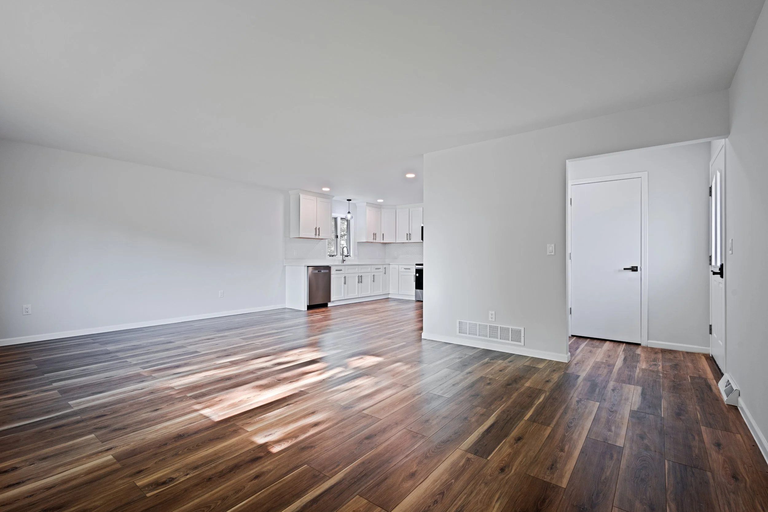 Empty living room and kitchen with white walls and wooden floors.