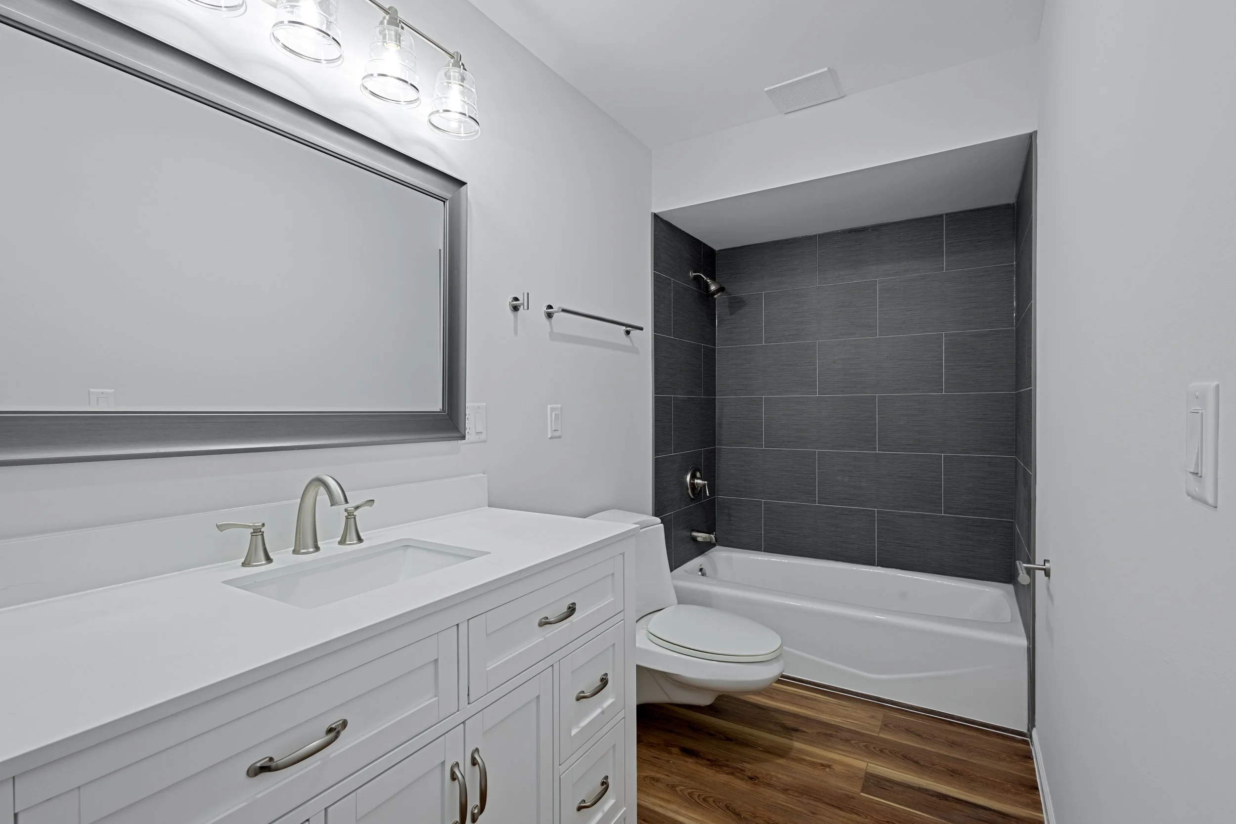 Modern bathroom with white vanity, large mirror, and black tiled shower with bathtub.