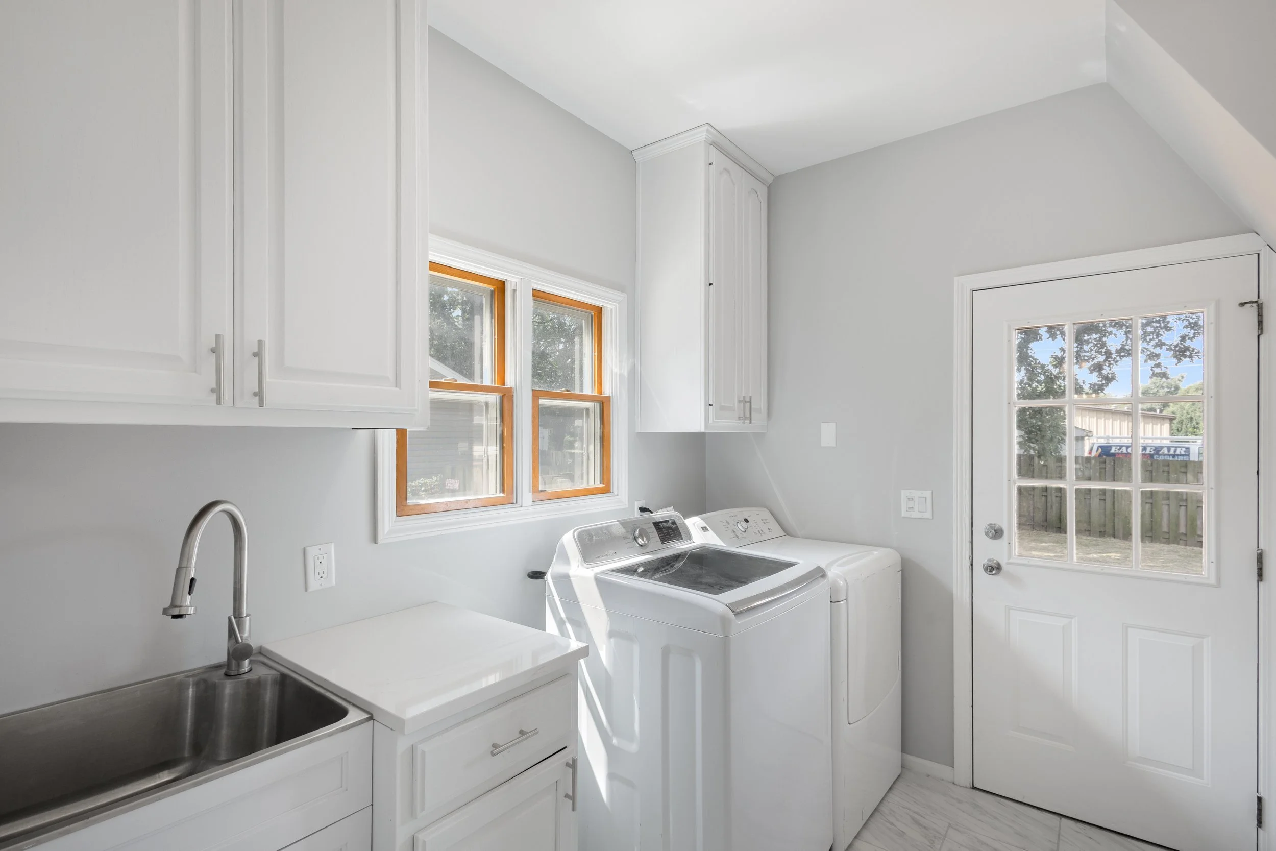Laundry room with white cabinets, a window, a sink, and a washing machine and dryer next to a door with glass panes