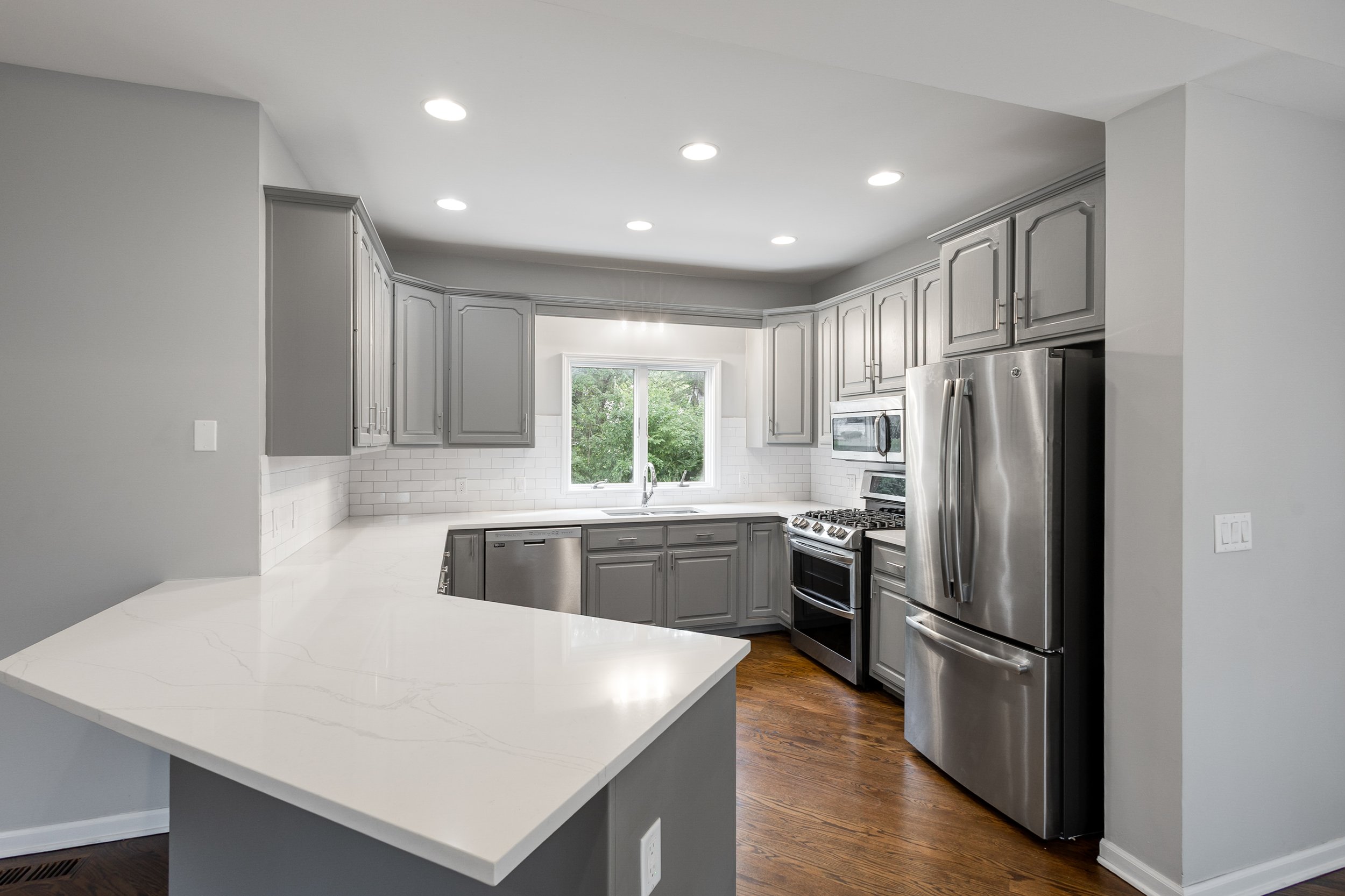 Modern kitchen with gray cabinets, white countertops, stainless steel appliances, and hardwood floors.