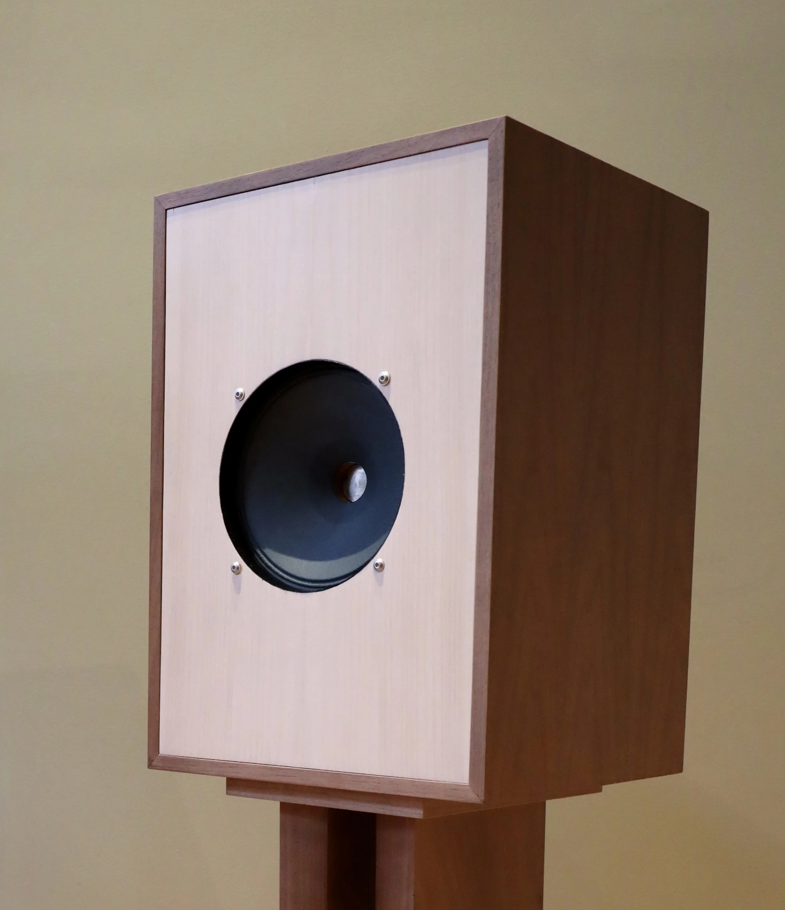 A wooden speaker on a stand with a black speaker cone in the center.