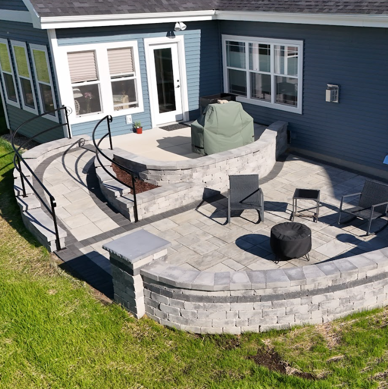 Hardscaping Job, backyard patio with stone retaining wall, outdoor furniture, and a covered grill next to a blue house