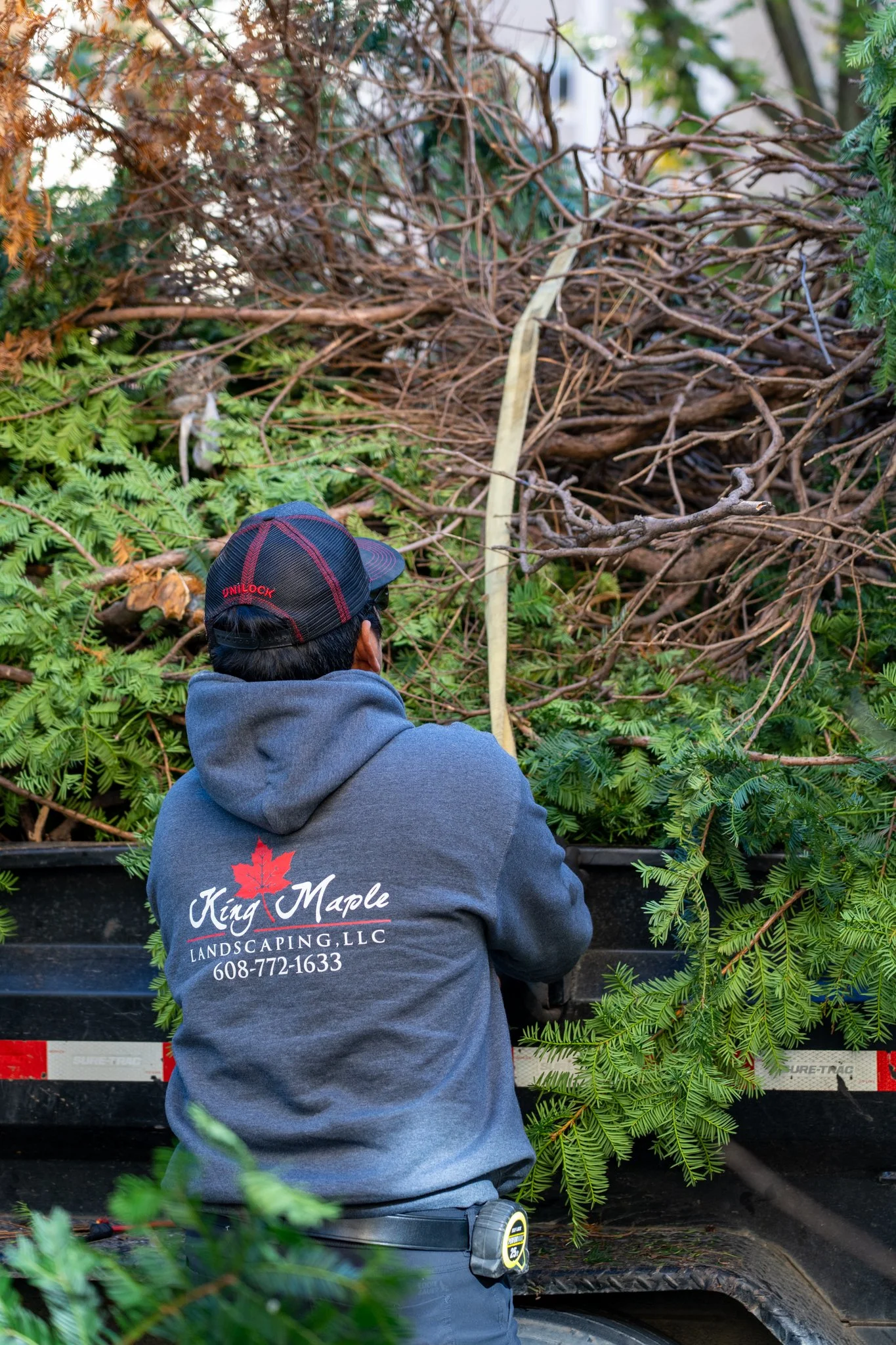 A King Maple Employee wearing a gray hoodie with the King Maple logo on the back, working with tree branches in the back of a truck.