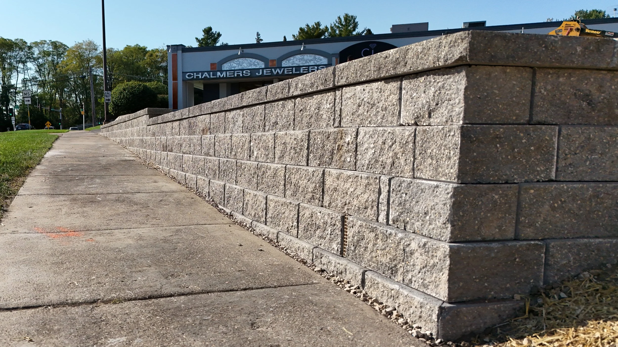 Close-up of a retaining wall installed by the King Maple Team, with a jewelry store named Chalmers Jewelers visible in the background.