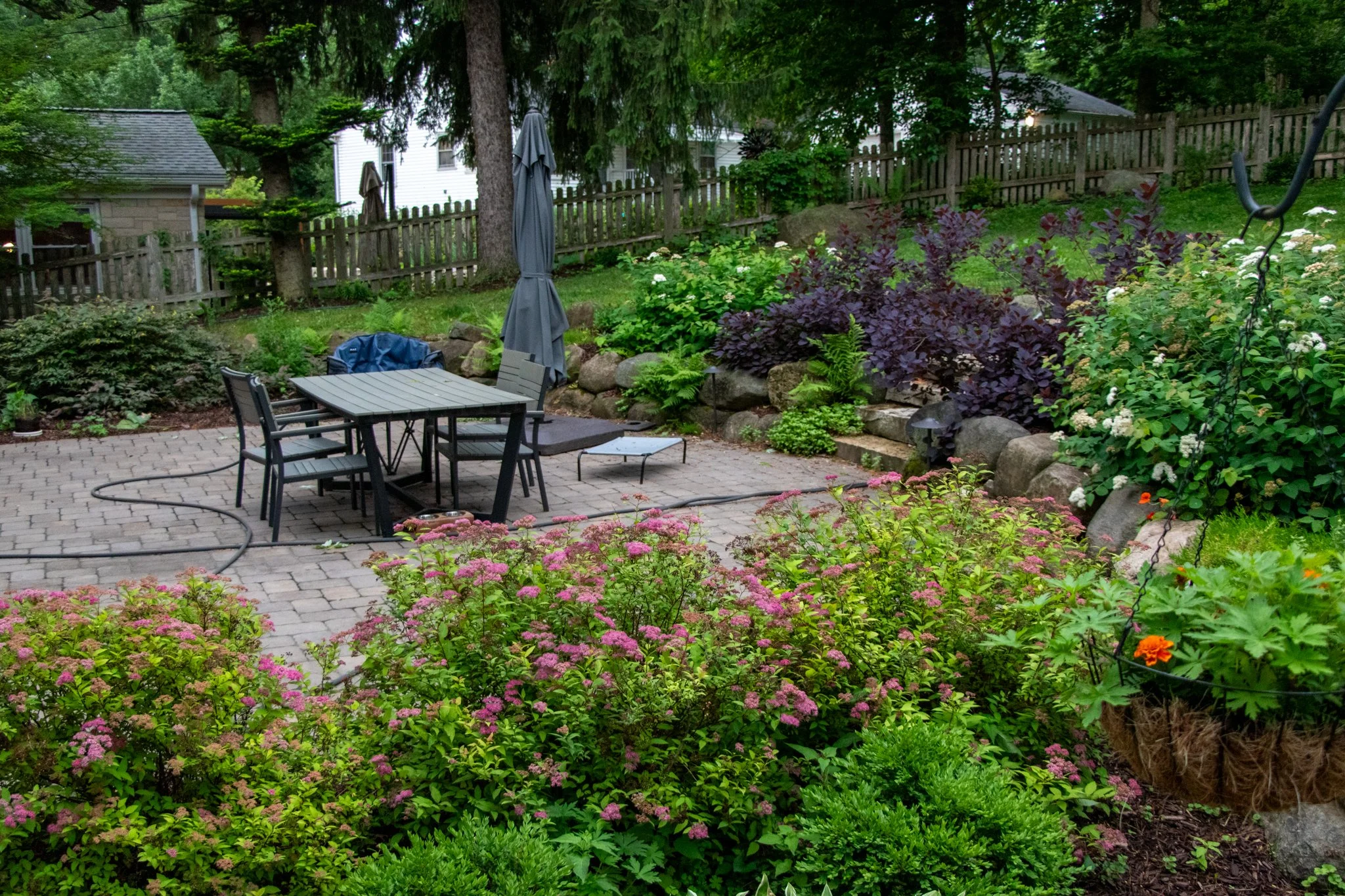 King Maple Hardscaping Project: Backyard garden with patio furniture, flowering plants, and a wooden fence in a lush, green setting.