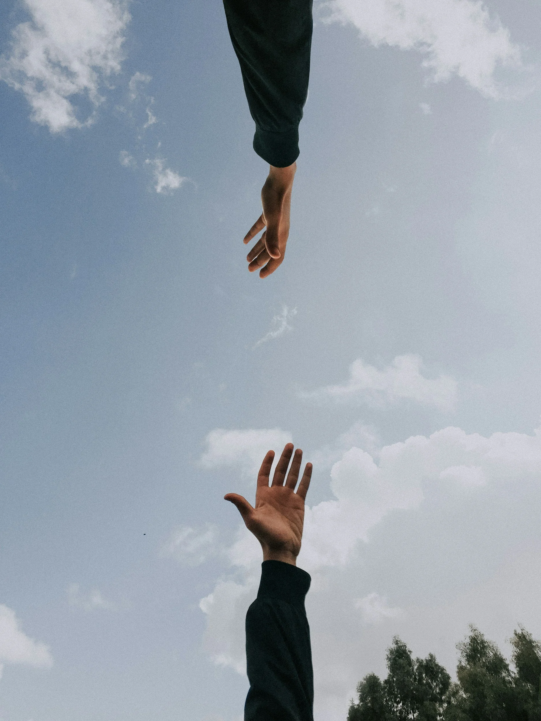 People reaching upward with hands, sky with clouds in the background.