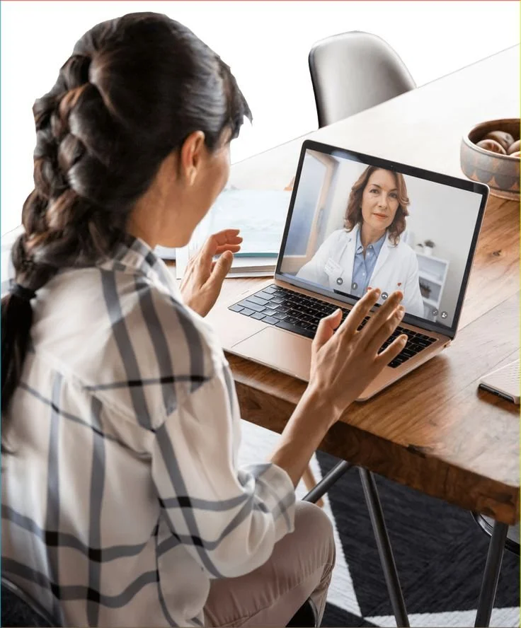 Woman in a plaid shirt having a video call with a female doctor on her laptop.