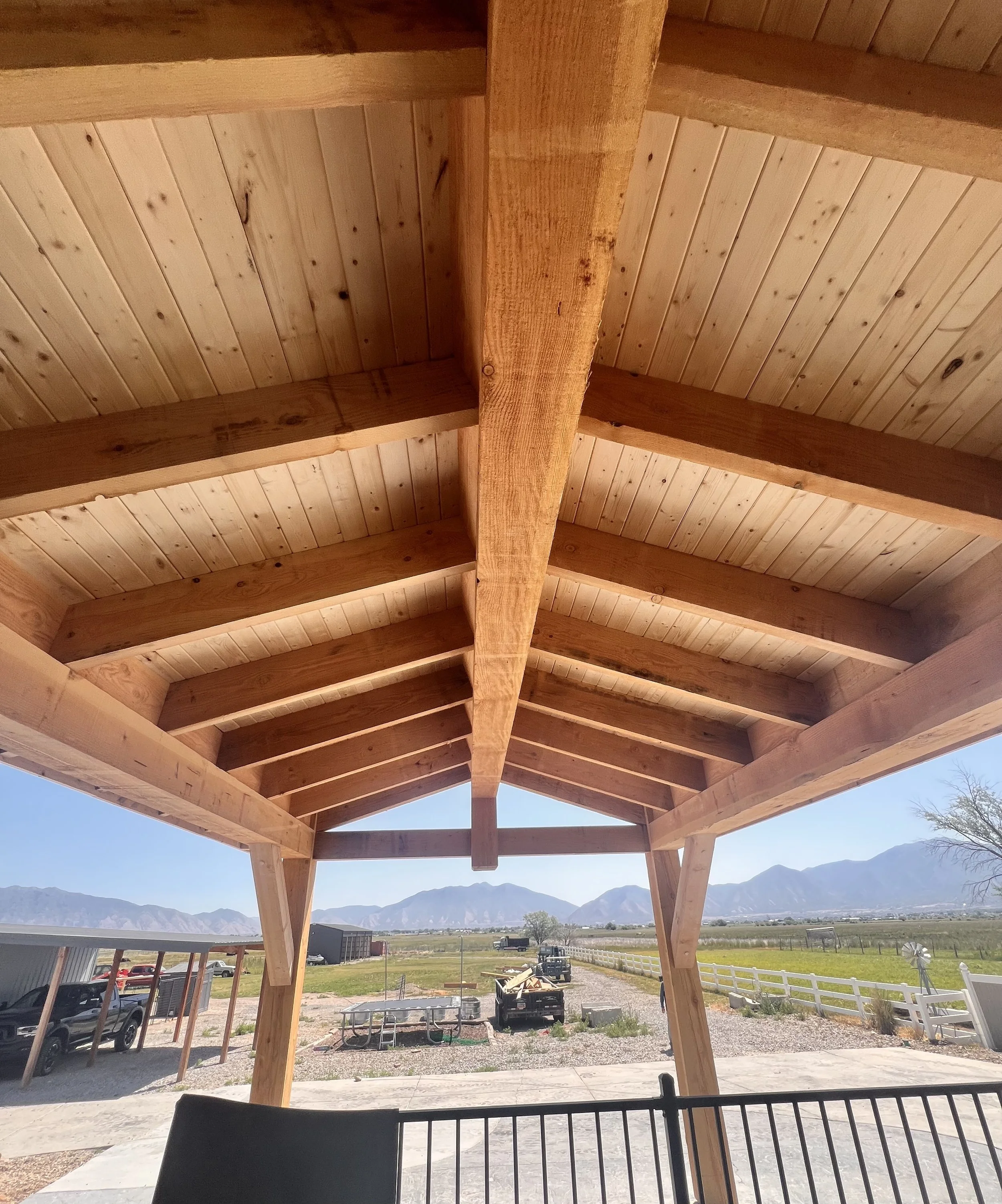 Looking up at a wooden porch ceiling with exposed beams, with mountains and open land in the background.