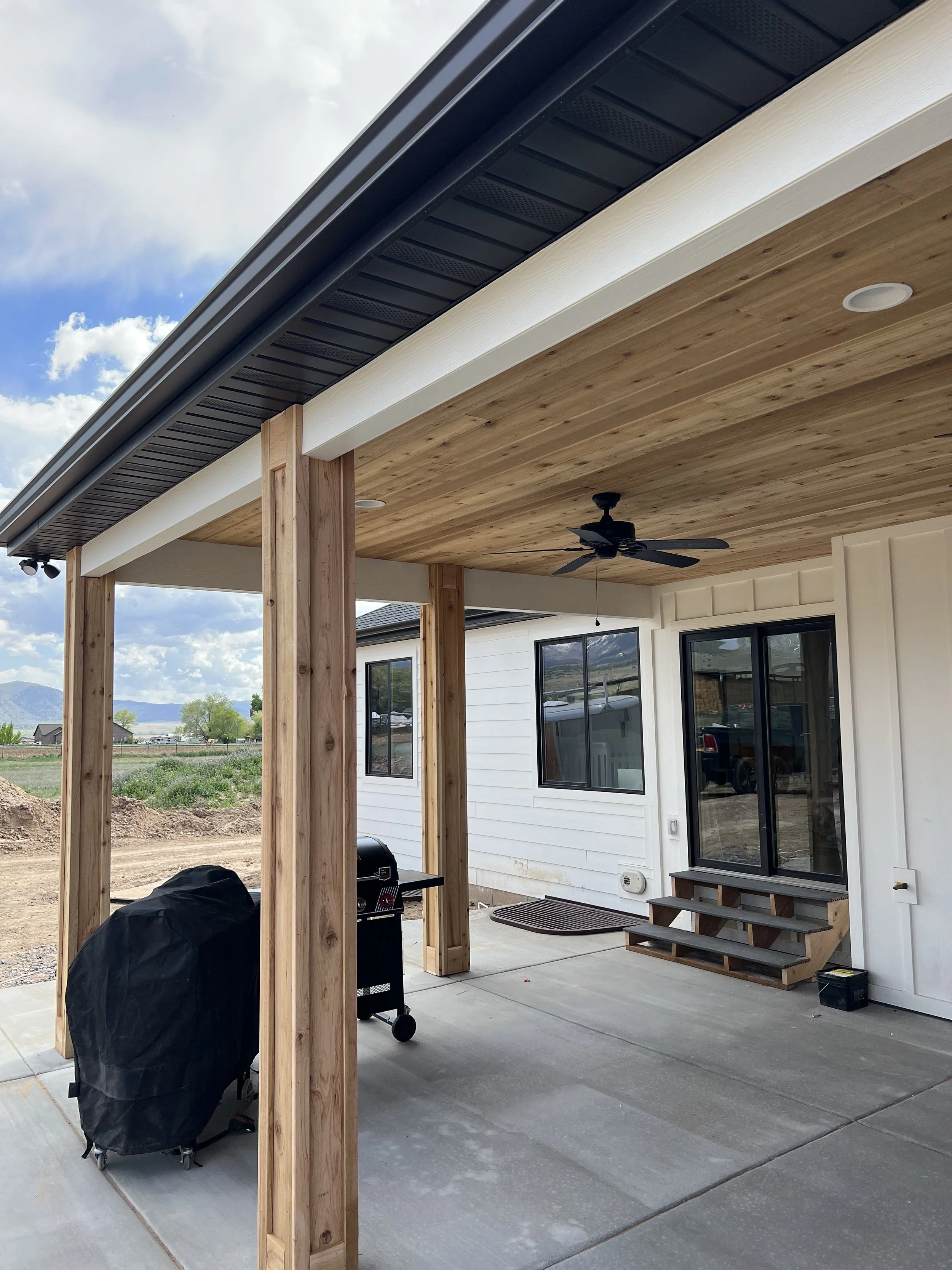 Newly built covered patio with wooden ceiling, ceiling fan, wooden support beams, sliding glass door, and outdoor steps leading to the backyard.