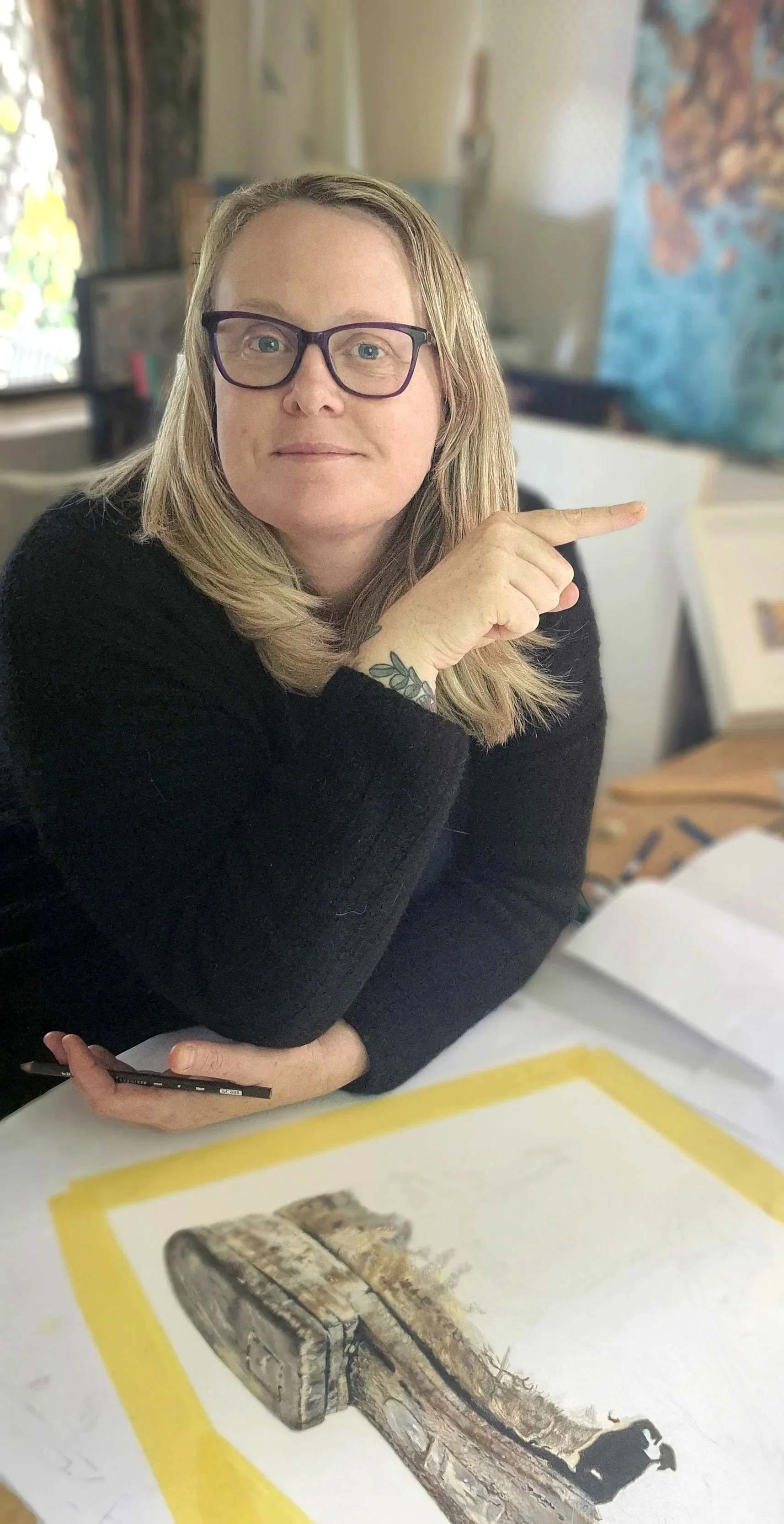 A woman with blonde hair and glasses pointing at a picture of an old boat or ship on a sheet of paper.