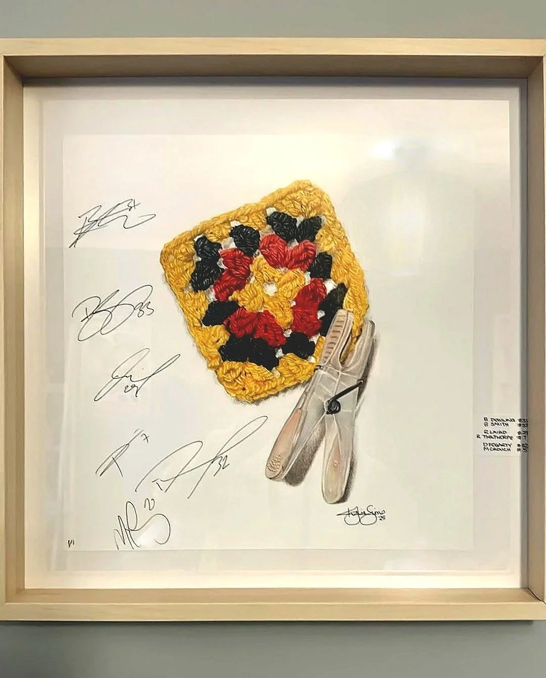 A framed embroidered artwork of a hockey puck with a floral pattern in red, black, and yellow, signed by various individuals.