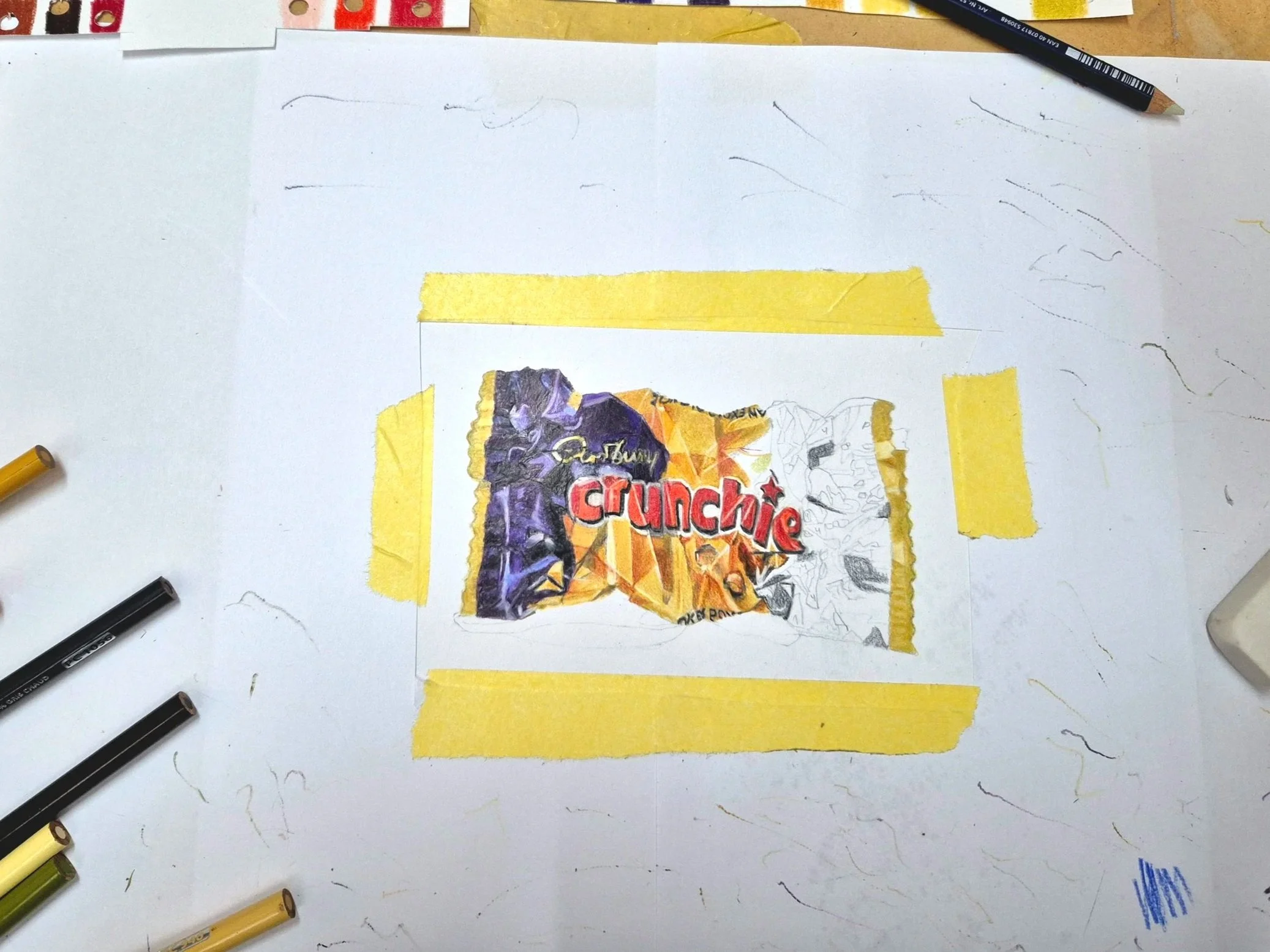 A worktable with a partially colored box of Crunchy Chips snack, surrounded by coloring pens, with a white sheet of paper underneath.