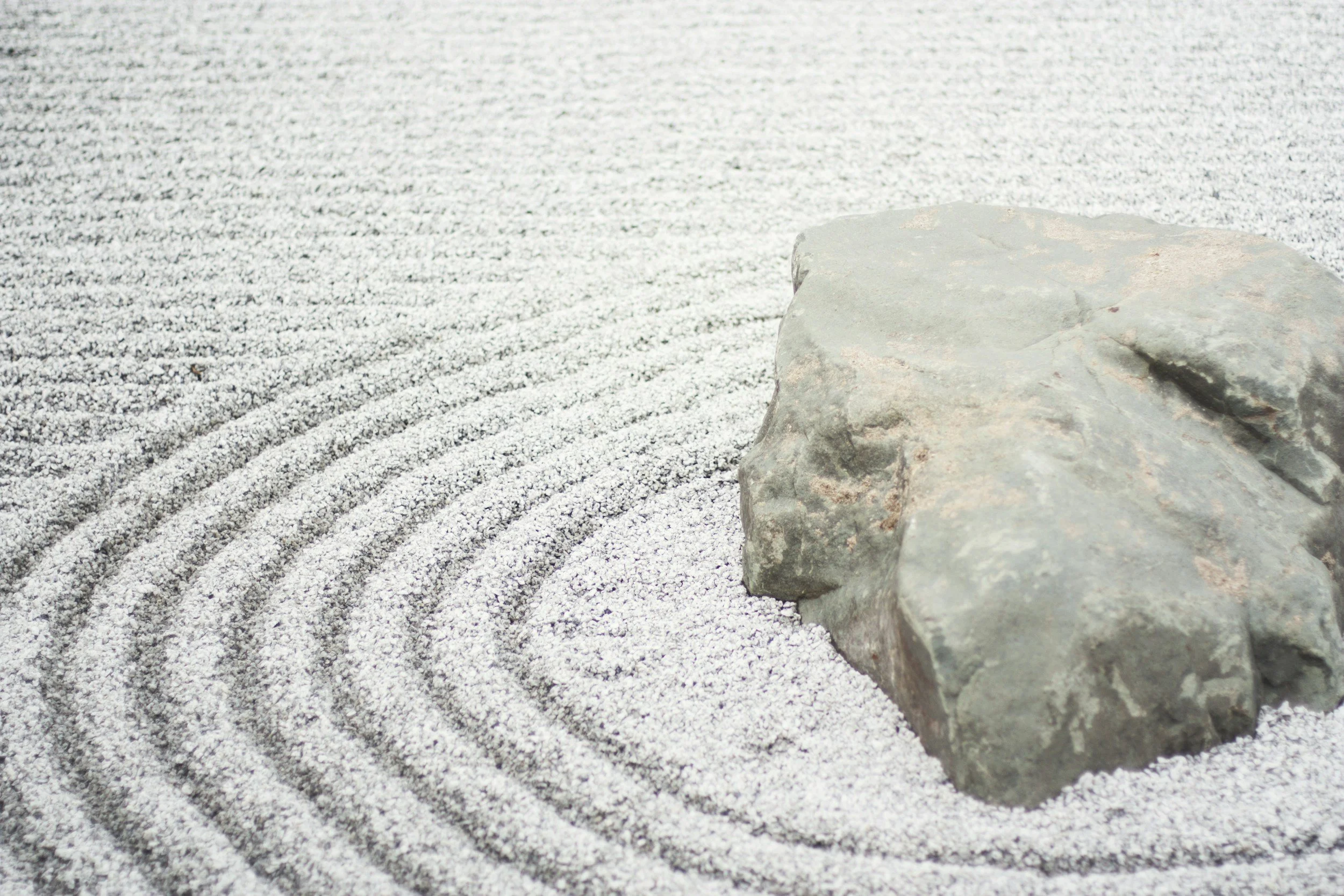 A Japanese Zen garden featuring a large gray rock surrounded by raked white gravel with concentric circles.