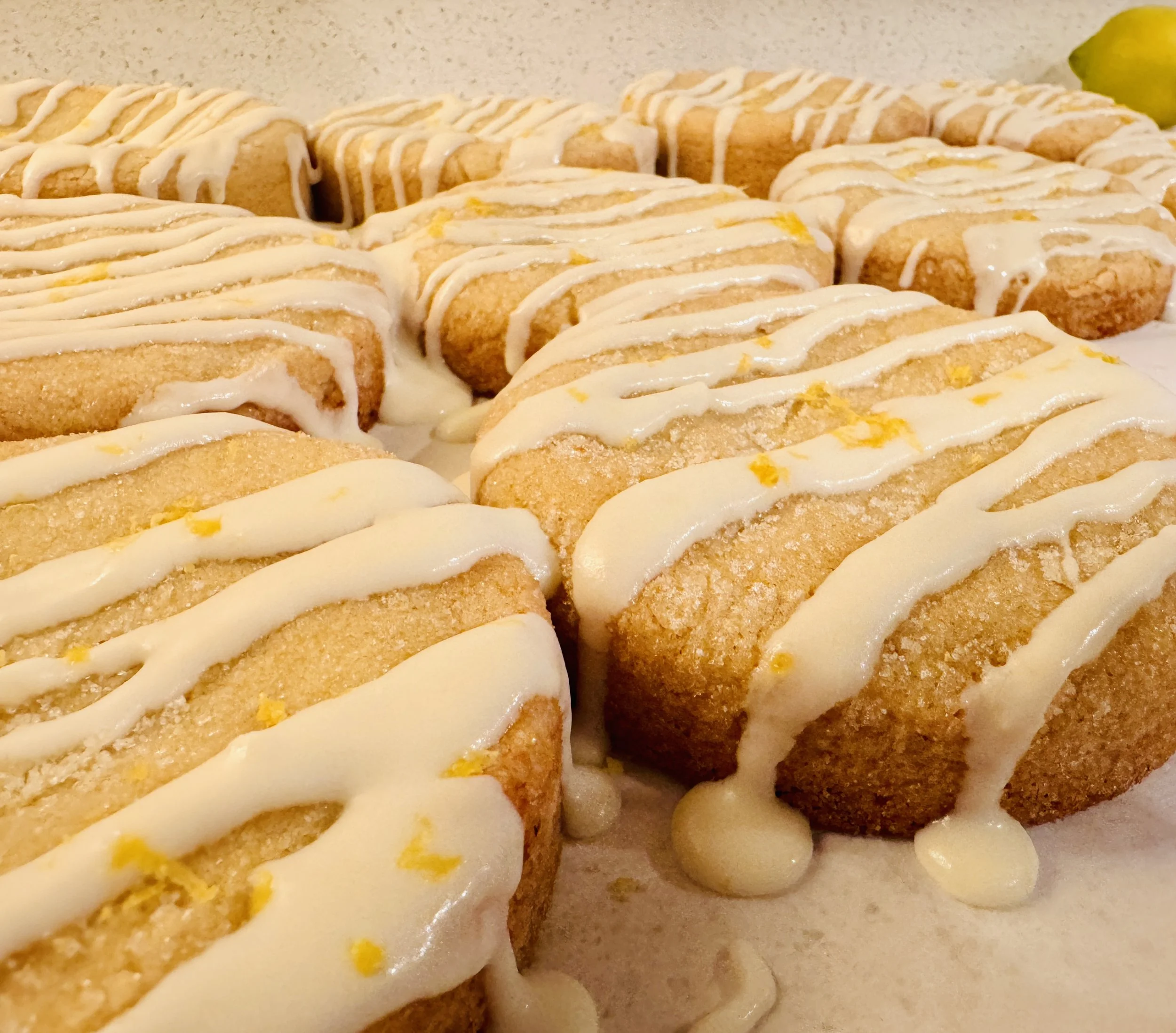 Close-up of rectangular lemon bars with glazed lemon topping and lemon zest, arranged on a parchment paper-lined surface with a lemon wedge in the background.