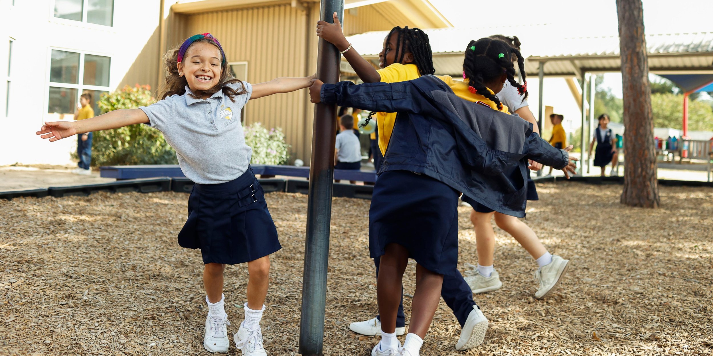 A group of young girls playing and holding hands on a playground, smiling and enjoying outdoor activities.