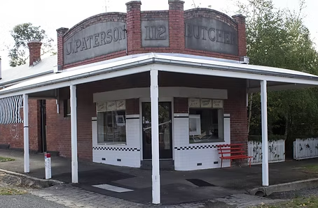 The exterior of a vintage brick building with a curved sign reading 'J. PATTERSON & CO. LITCHFIELD' and a white porch with red bench, black and white checkered floor, and large windows.