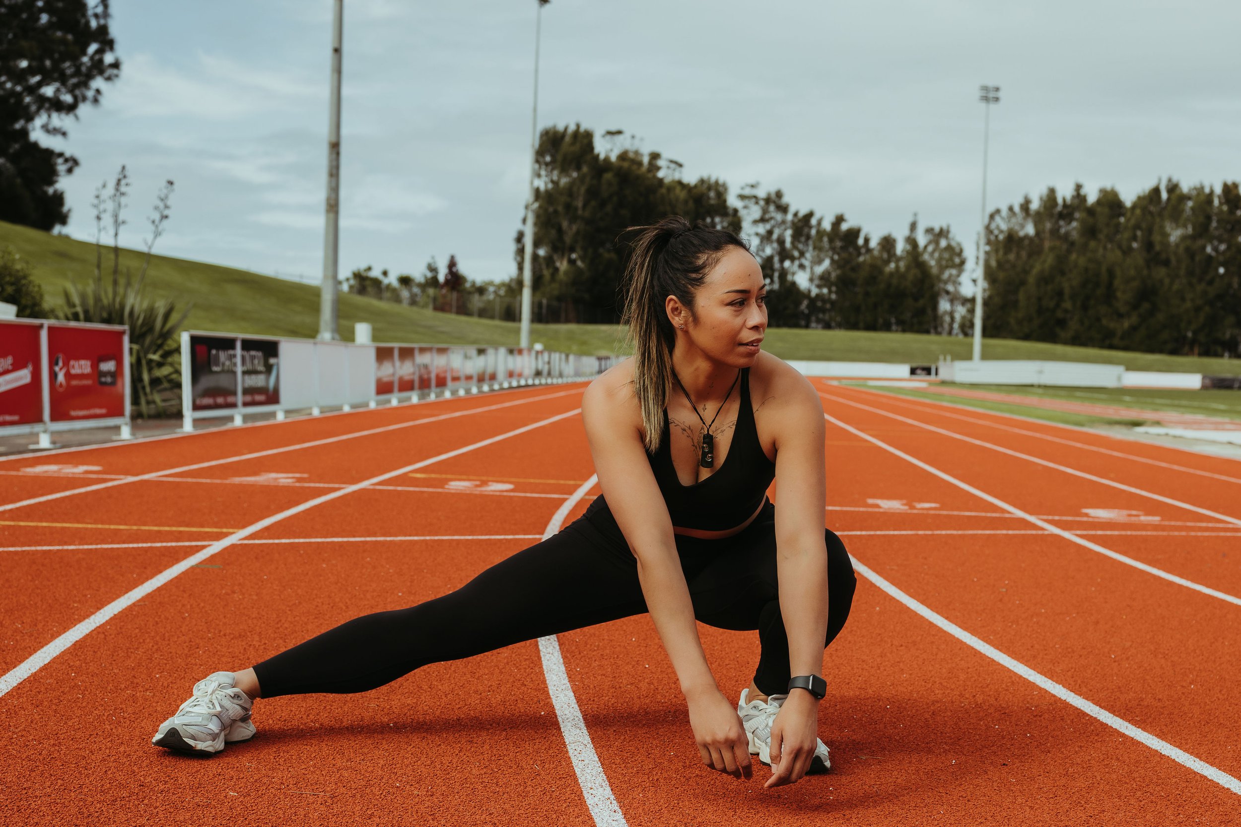 māori women doing a leg stretch on a running track