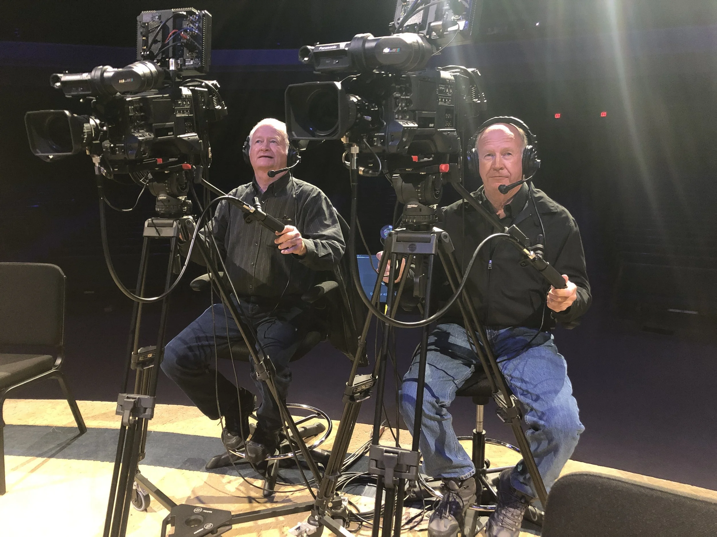 Two men in black shirts operating video cameras in a studio.