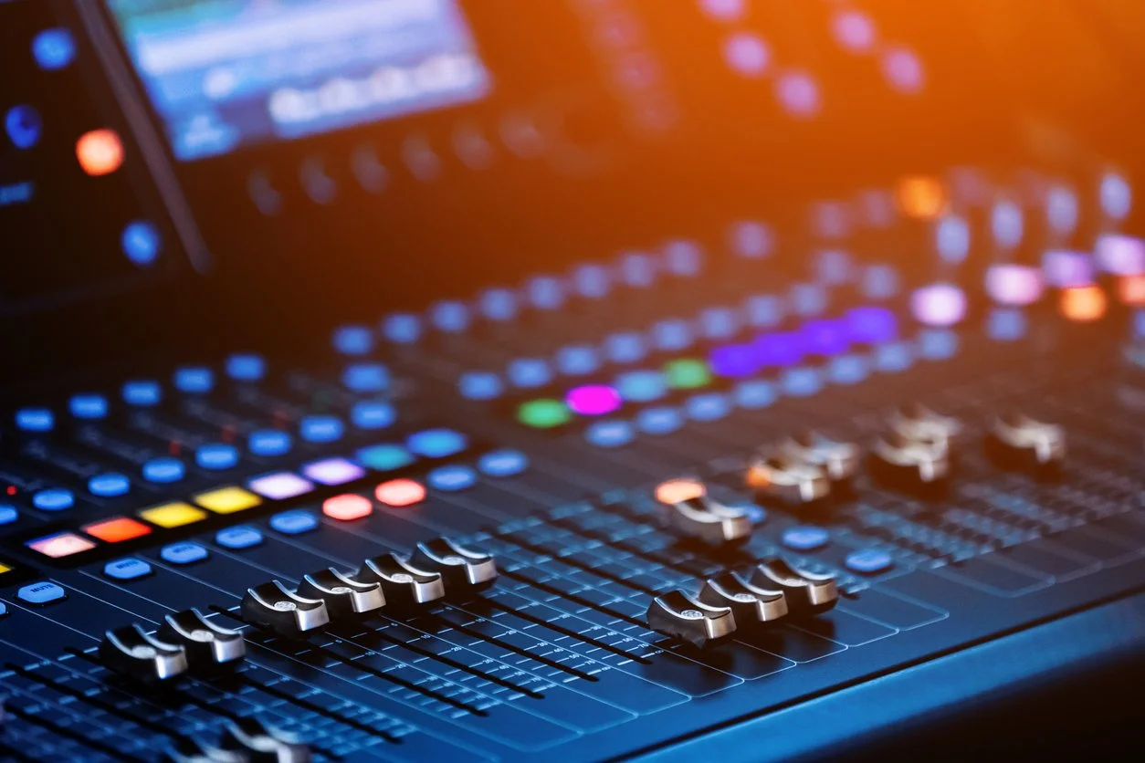 Close-up of a digital audio mixing console with illuminated colorful controls and sliders.