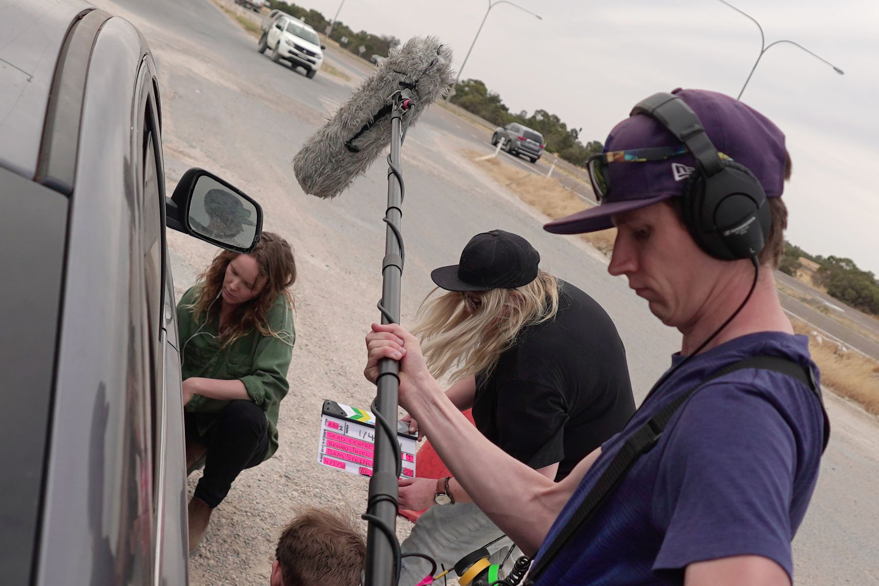 Behind-the-scenes shot of location sound recordist Alistair Schmidt capturing audio with a boom mic during a vehicle scene for Dead Centre.