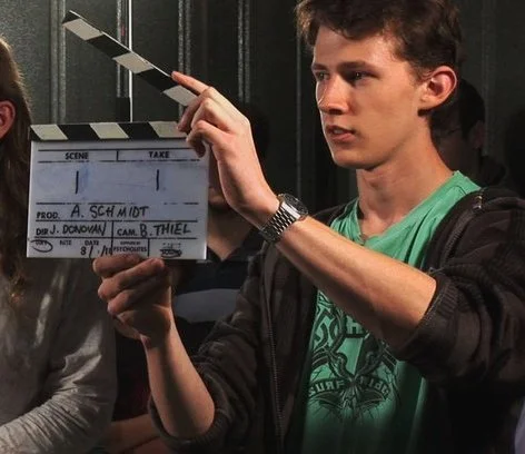 Filmmaker Alistair Schmidt holding a production clapperboard slate on set.