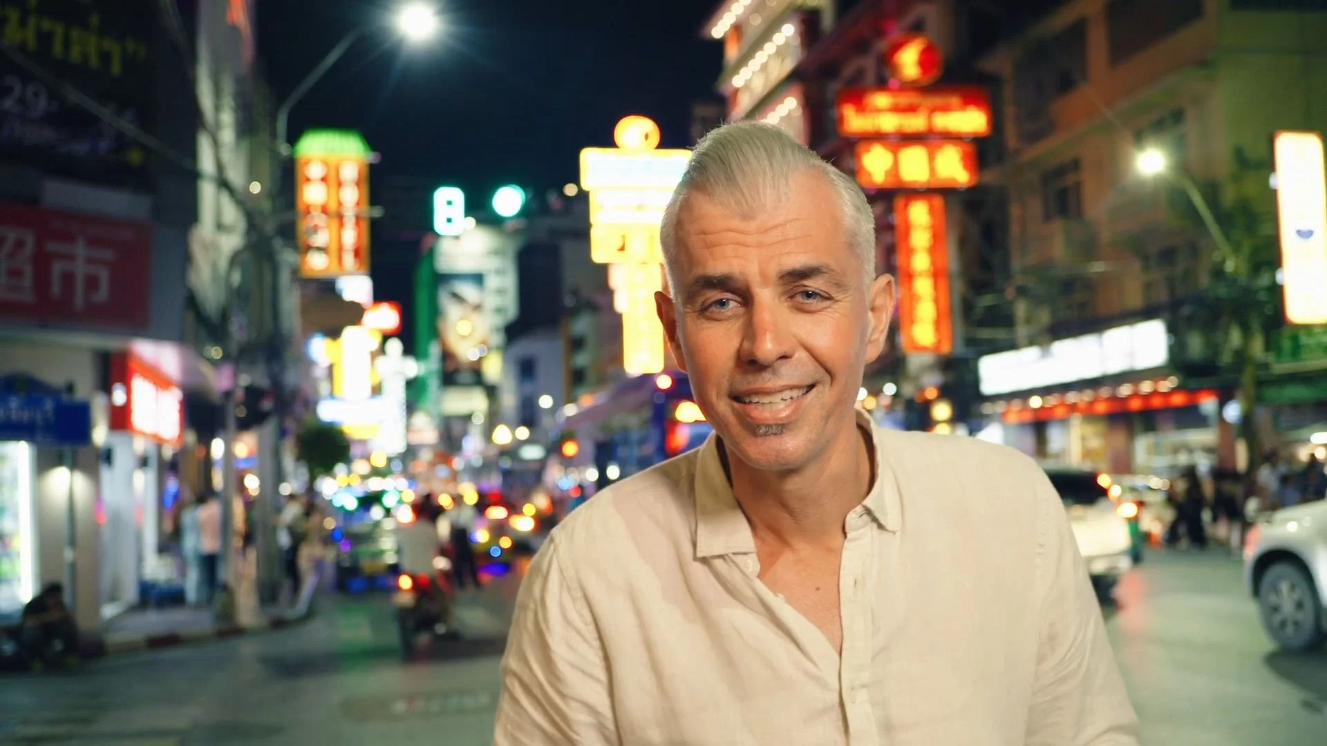 TAV Productions' Spaghetti Conquest host Adam Swanson, pictured during night filming on a bustling street with blurred neon signs.