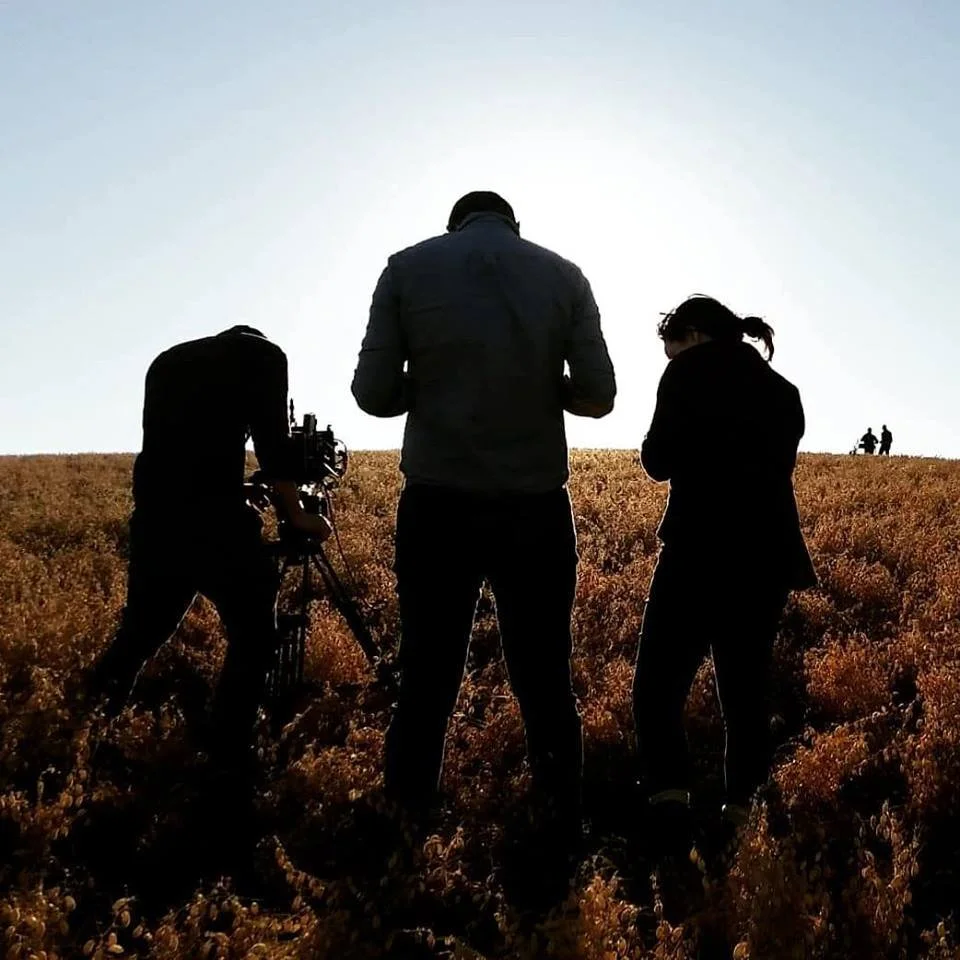 Behind-the-scenes silhouette of Director Benno Thiel's crew shooting the short film 'Where We Began' at golden hour in an open field.