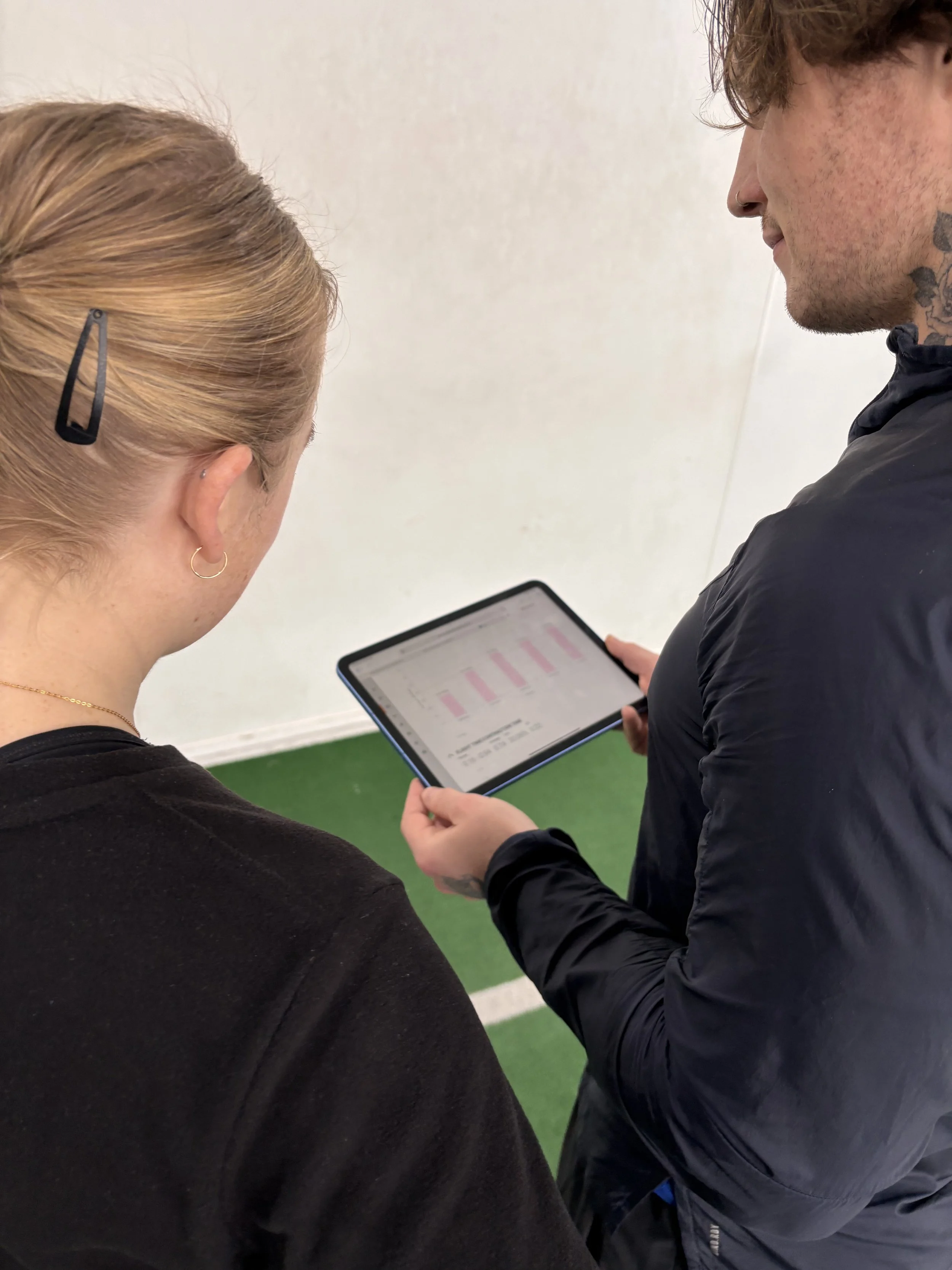 A woman and a man are standing together looking at a tablet screen displaying a bar graph, looking at objective testing data for a combat athlete.