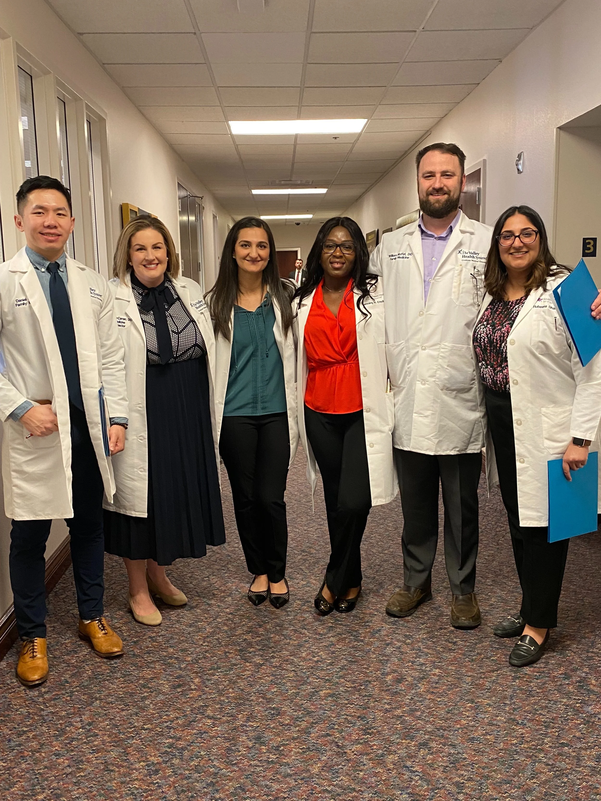 Dr. Dhami and a group of five other diverse medical professionals from her residency program wearing white coats and standing in a Nevada capitol hallway.
