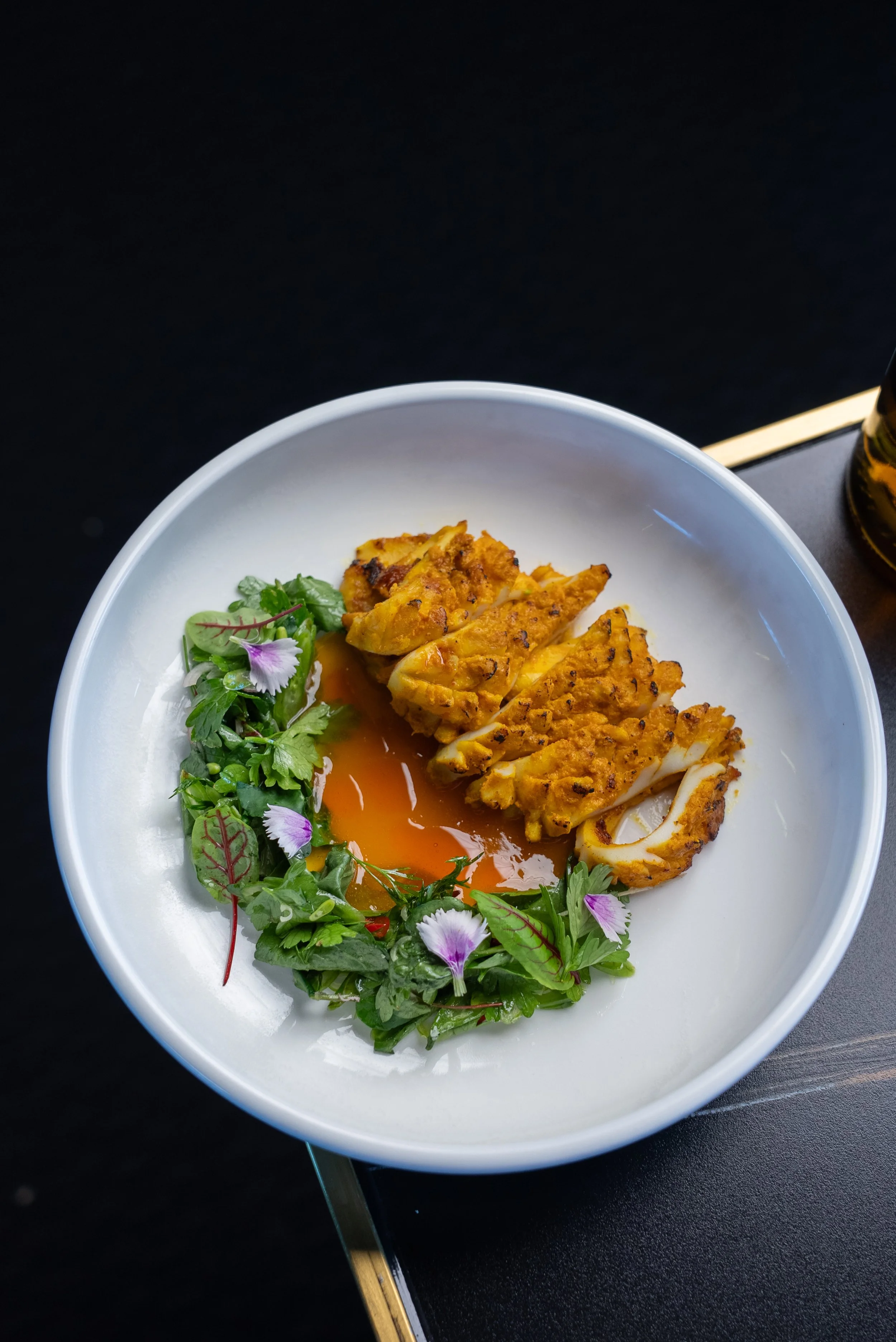 Sliced grilled chicken served with a salad of mixed greens and edible flowers with a soft-boiled egg in a white bowl.