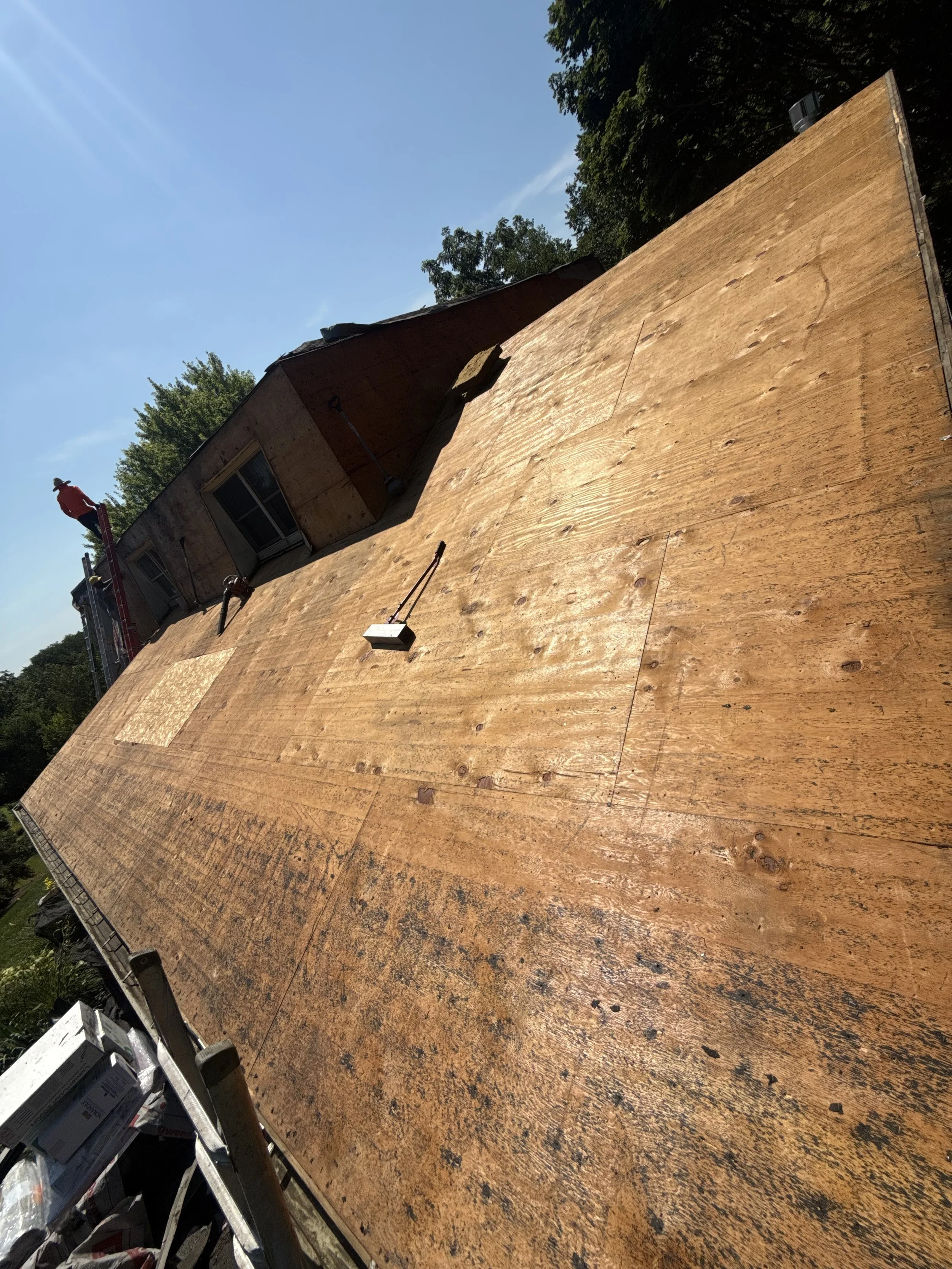 Construction worker on a house roof under construction, with plywood sheathing, after installing the decking.