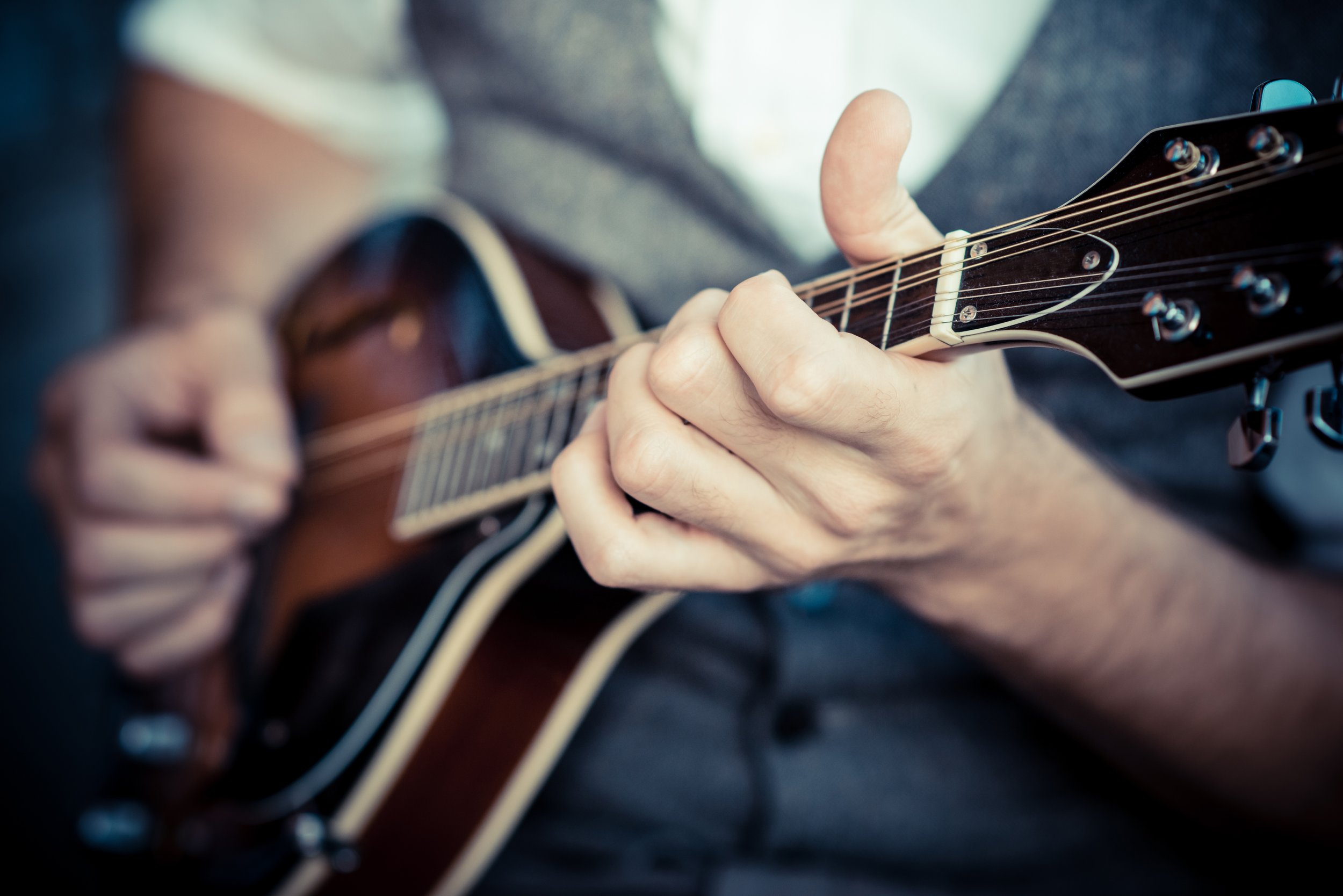 Close-up of a person’s hands playing an acoustic guitar, with fingers on the fretboard.