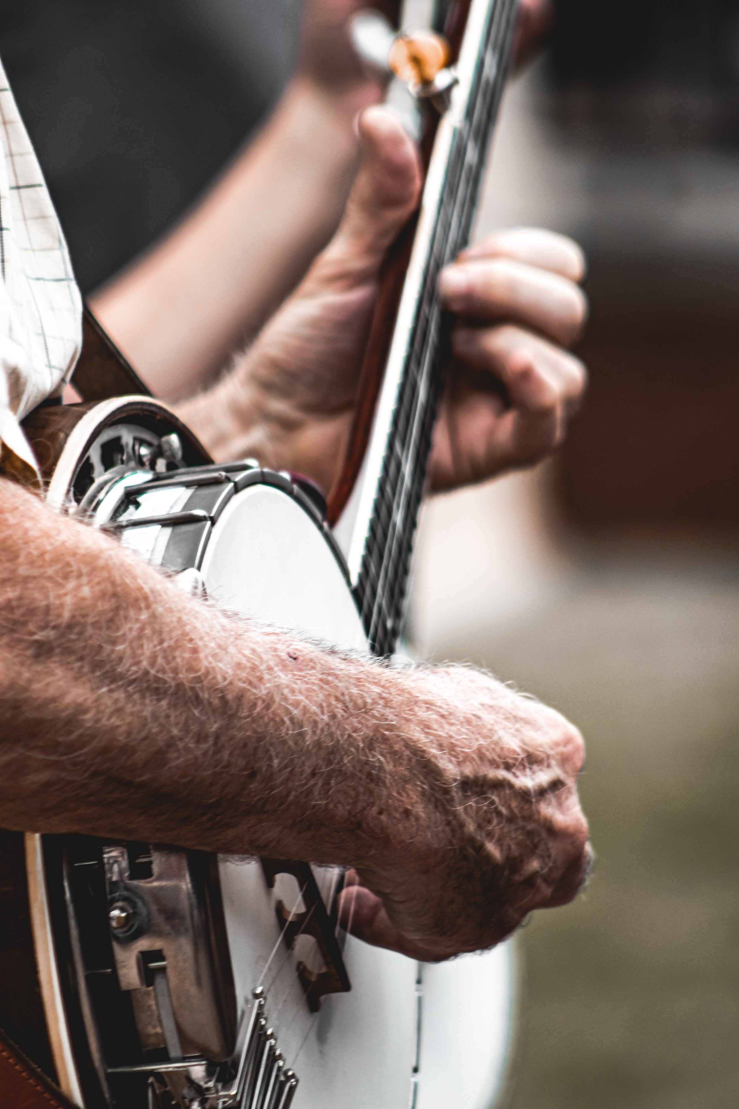 Close-up of an elderly person's hand playing an acoustic guitar. The hand is positioned on the fretboard, pressing down on the strings.