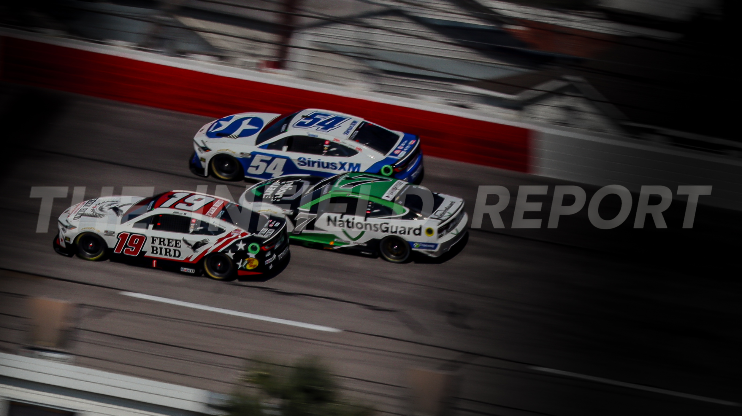 Three race cars on a track, with a red and white barrier and blurred background, numbered 19, 54, and 12, featuring logos for SiriusXM, NationsGuard, and other sponsors.