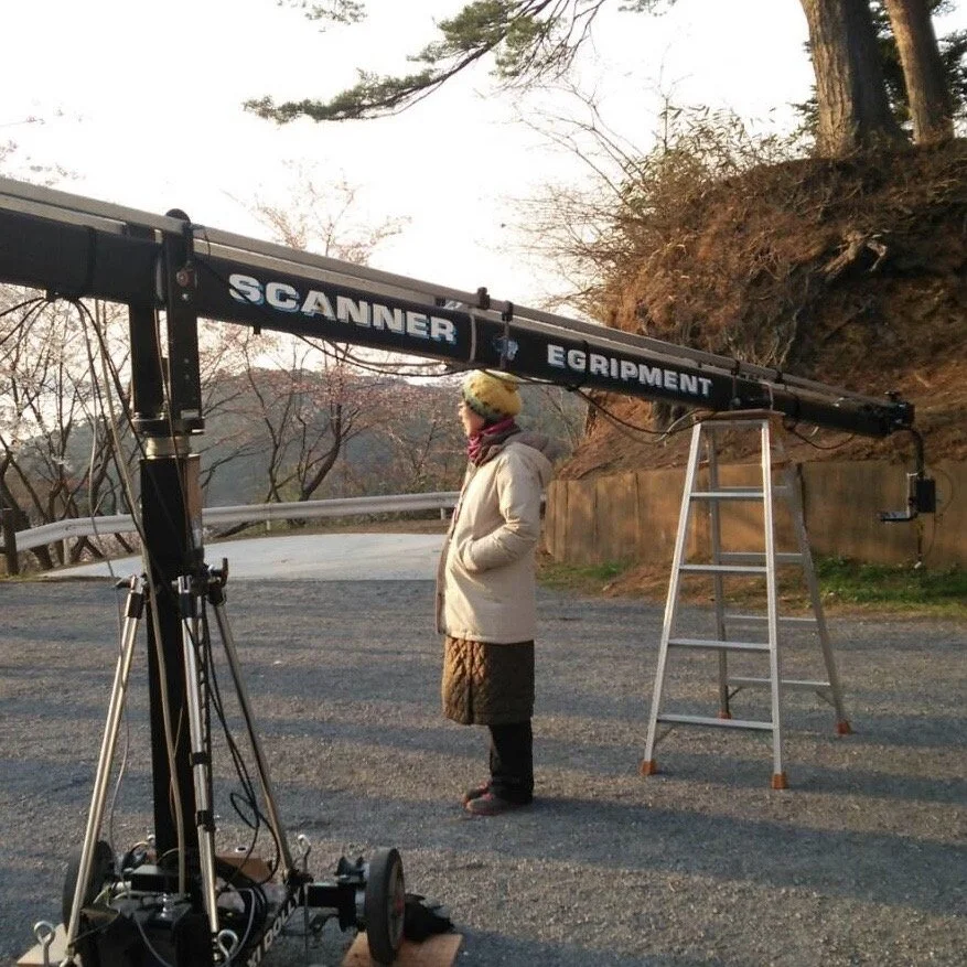 Person standing beside camera equipment on a rural road in Japan.