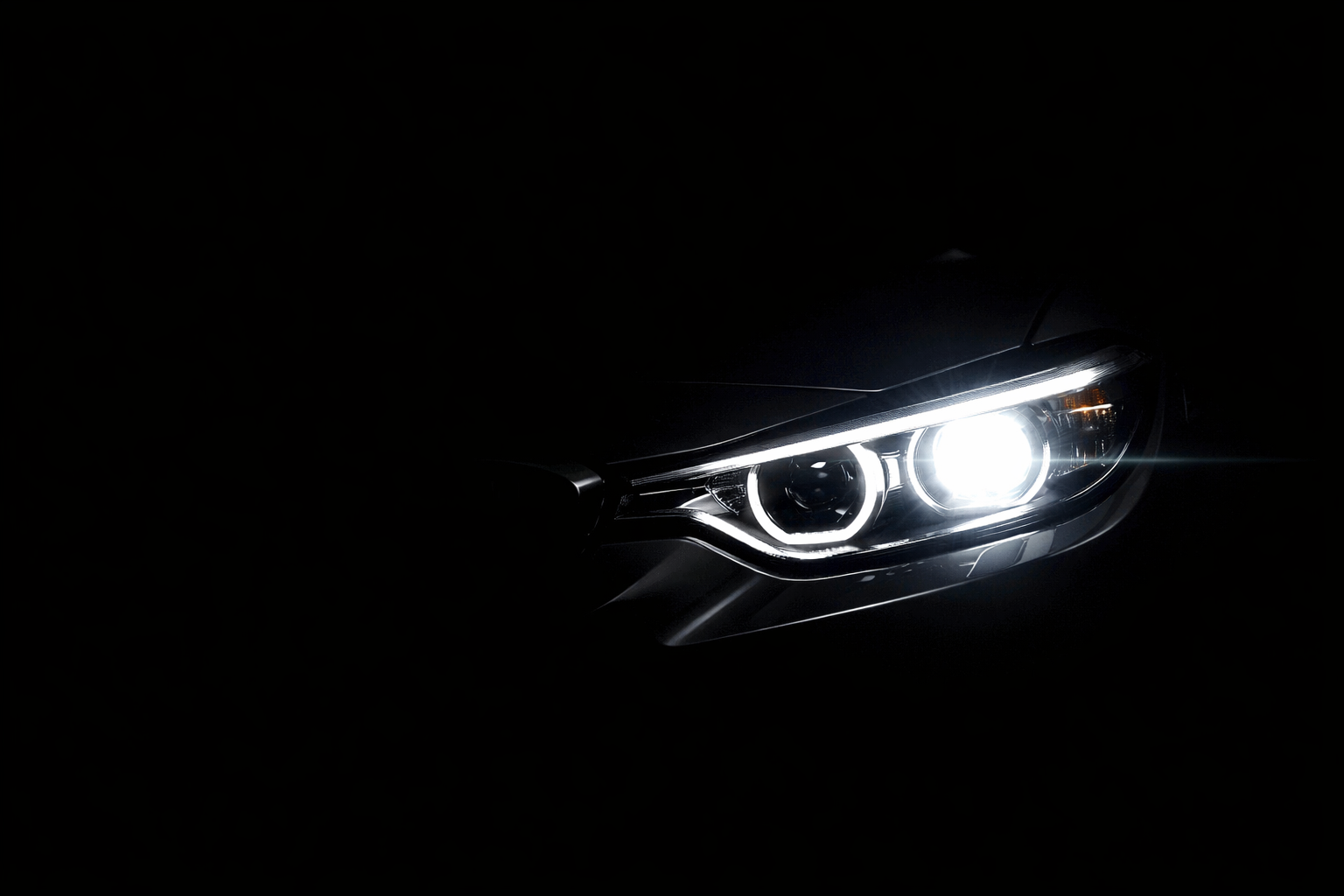 Close-up of a car's headlight illuminated in darkness.