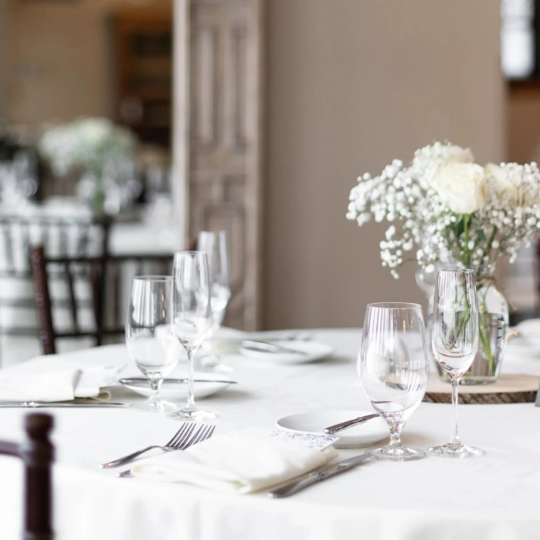 A dining table set with wine glasses, silverware, and a floral centerpiece in a well-lit room.