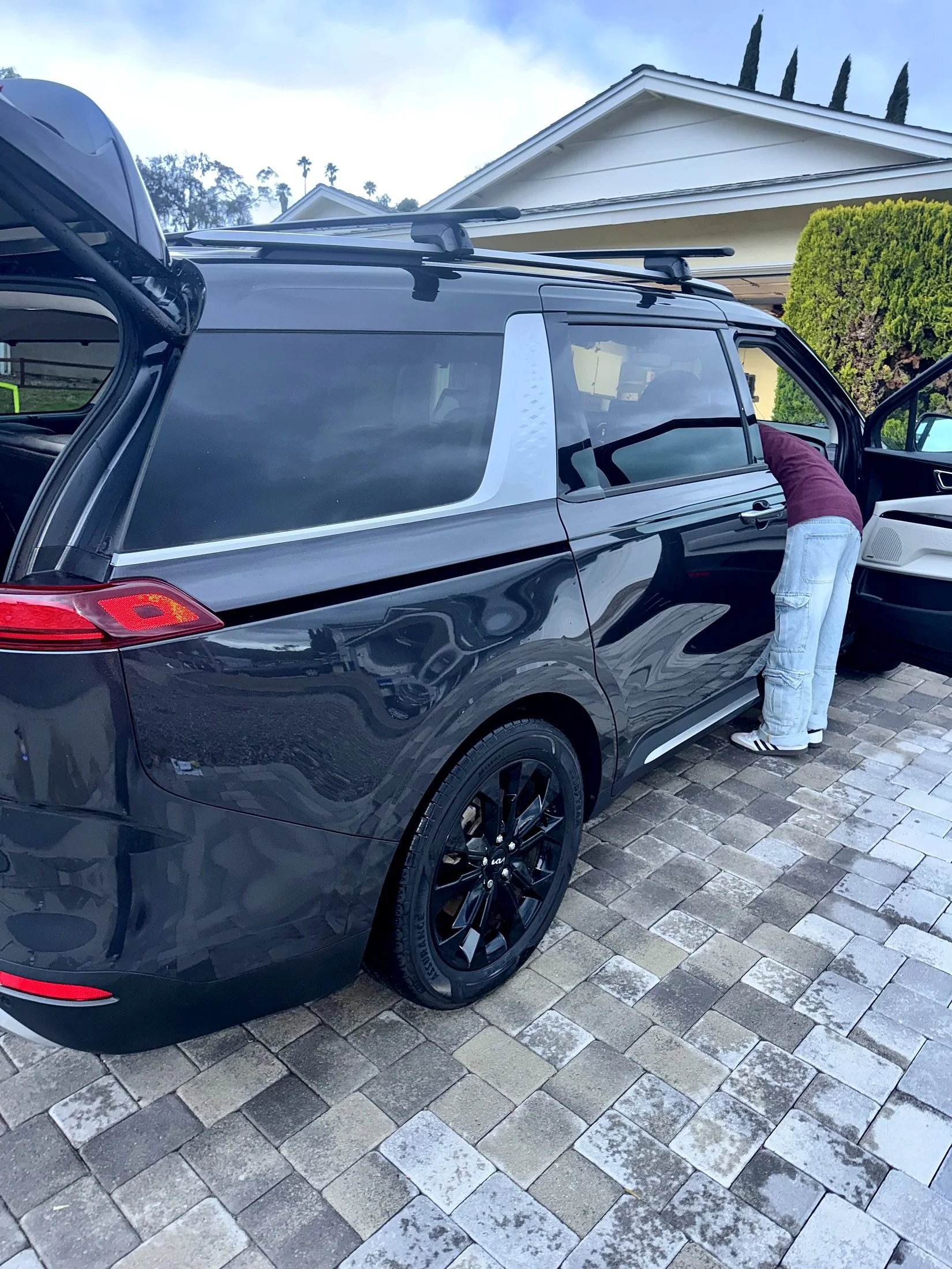 Santo's Suds crew detailing a black Kia Carnival in a customer's driveway