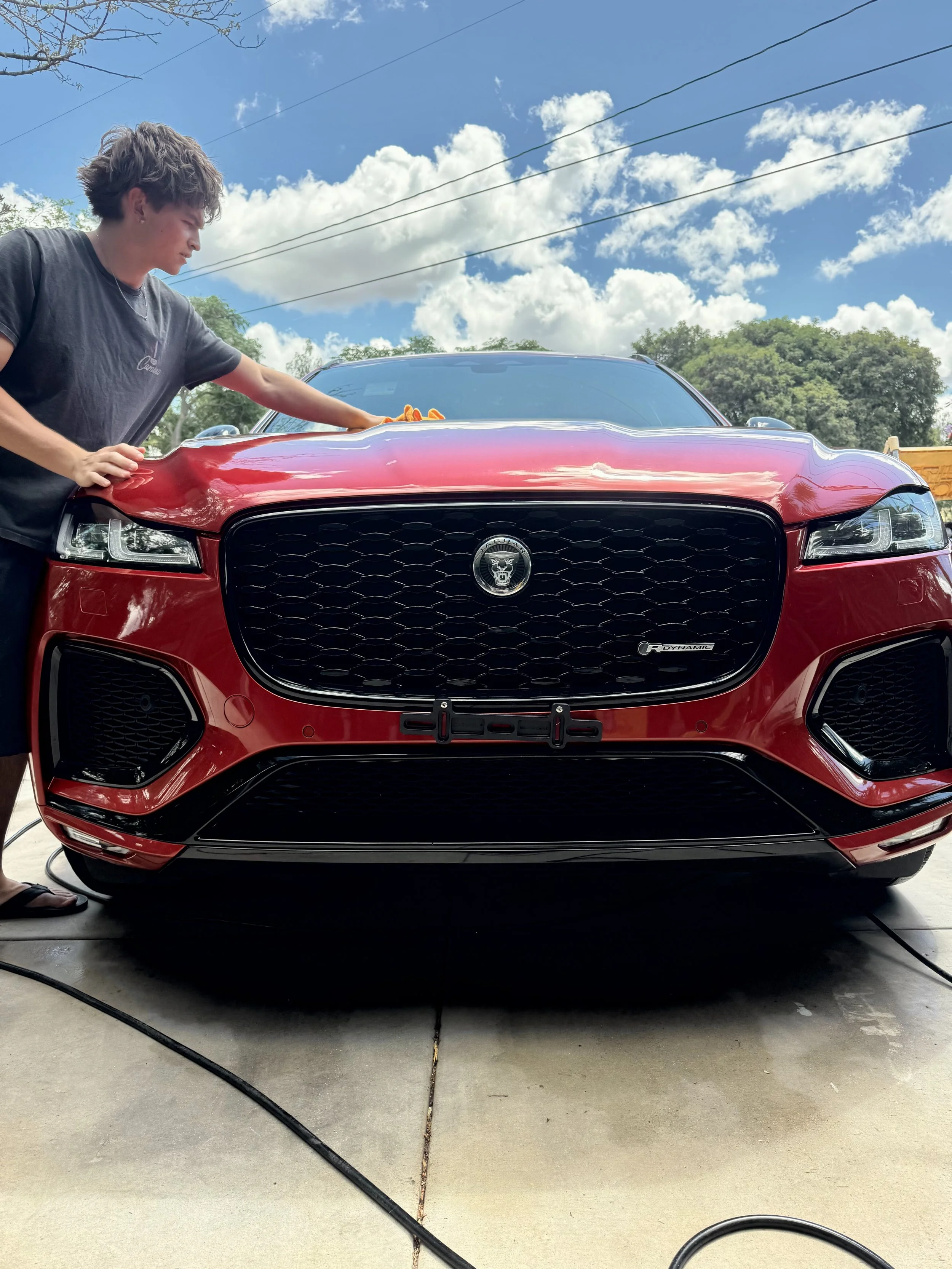 Santo's Suds detailer hand washing a red Jaguar F-Pace in a customer's driveway